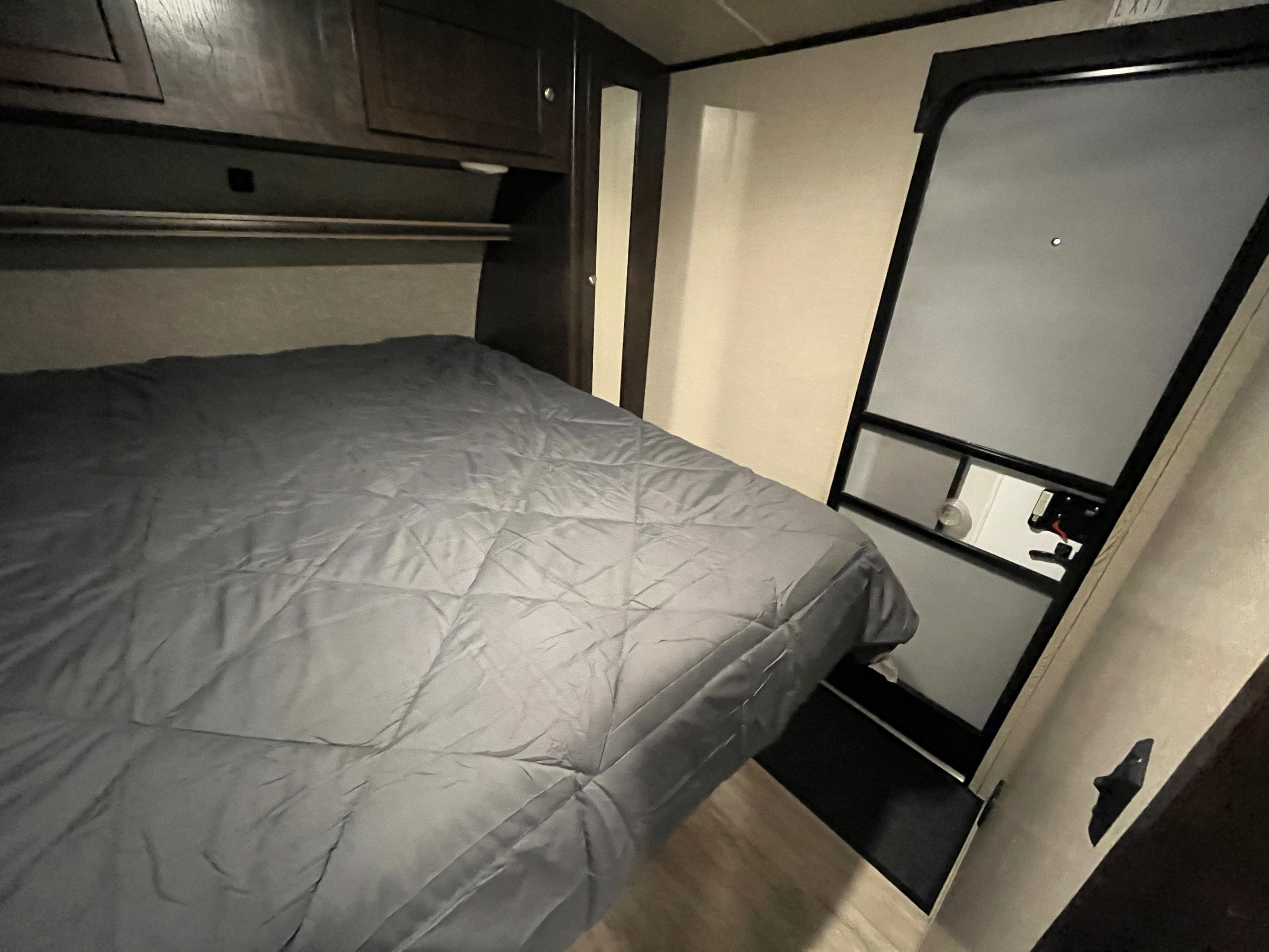 Cozy rv rental bedroom featuring a grey bed, overhead storage, and a partially open exterior door, ready for your adventure.. Cruiser RV Shadow Cruiser 2018