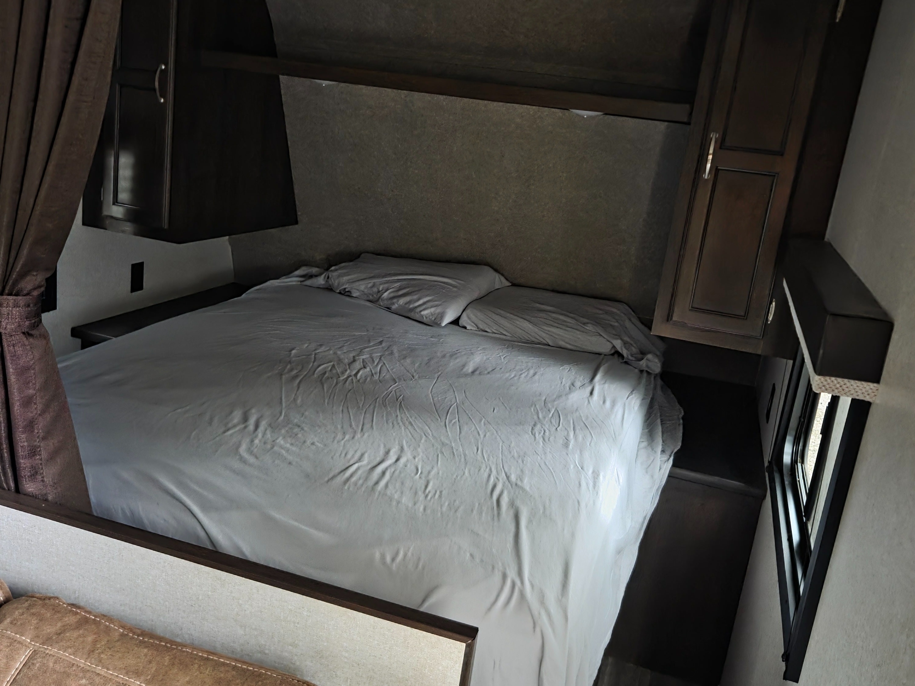 An RV rental's compact bedroom showing a bed with grey sheets, dark cabinets, and a window.. Jayco Jay Flight 2018