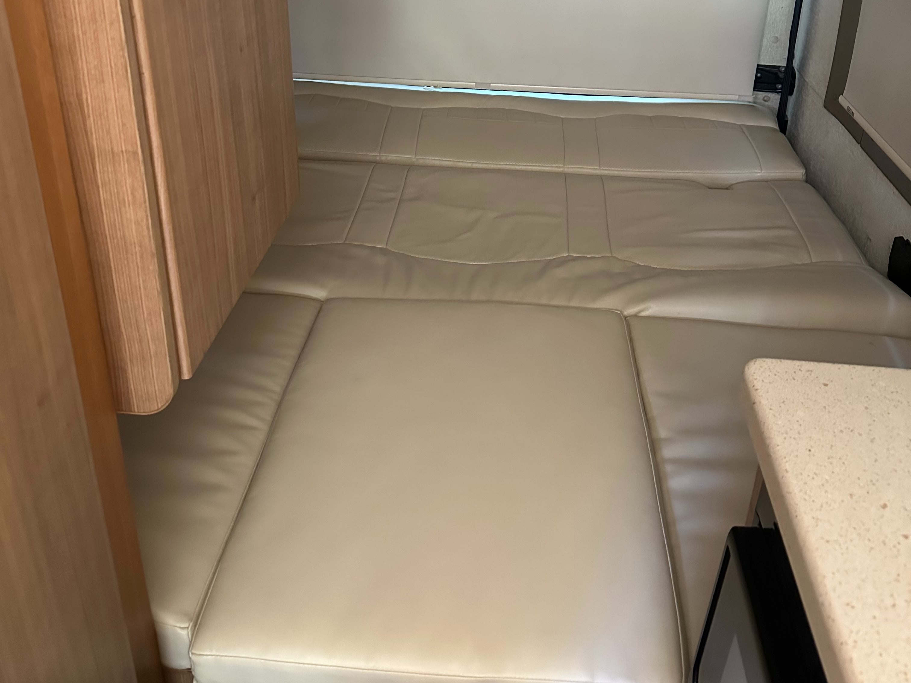 RV rental's cozy sleeping area with light, flat cushions, wooden trim, and a small countertop. Ideal for rest.. Winnebago Era 2013