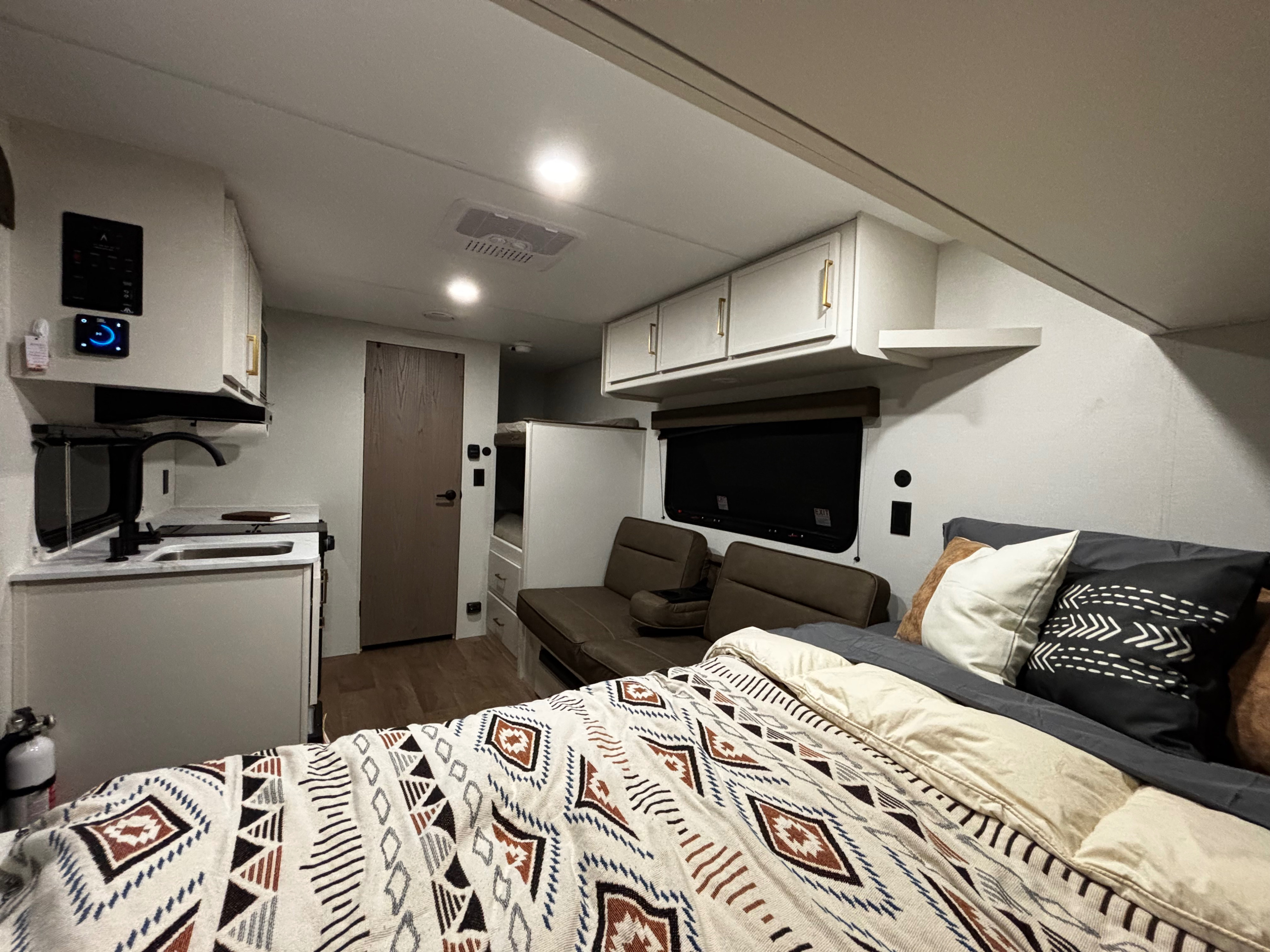Cozy rv rental interior: main bed in foreground, compact kitchen, sofa, and bunks visible. Well-lit and functional.. Grand Design Transcend One 2027