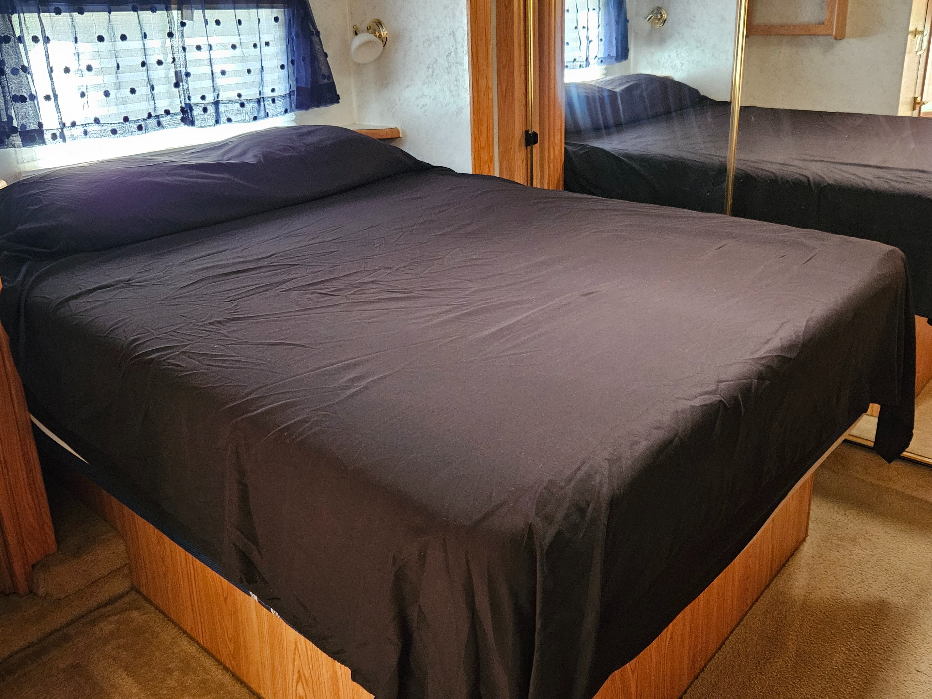 Comfortable dark blue bed in an RV rental, with polka-dot curtains and mirror reflection in the compact bedroom.. Cedar Creek Cedar Creek Fifth Wheel 2002