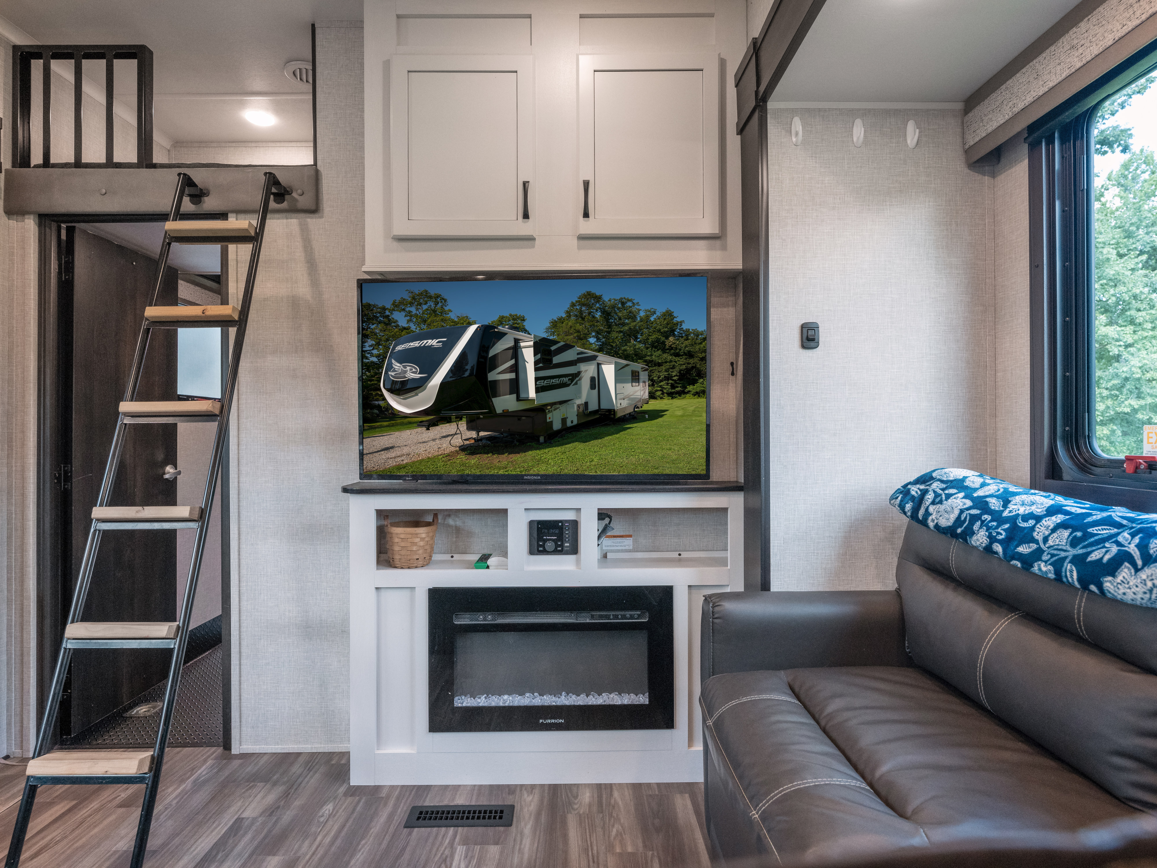 Modern RV rental living area featuring a loft bed, TV, electric fireplace, and comfy couch.. Jayco Seismic Luxury Toy Hauler 2024