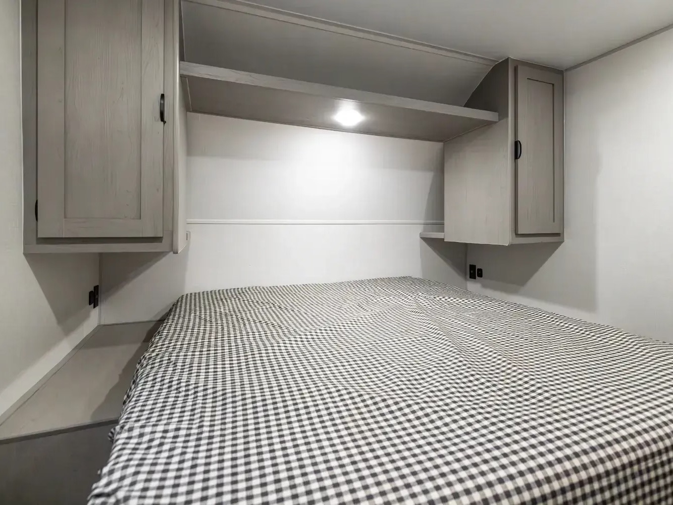RV rental bedroom interior: a comfy bed with checkered bedding, overhead cabinets, and shelves. Perfect for a cozy night on the road.. Forest River Viking 6k 292TB 2025