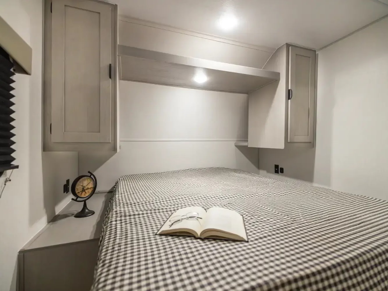 **RV rental** bedroom featuring a checkered bed, overhead cabinets, reading light, book, and a small clock.. Forest River Viking 6k 292TB 2025