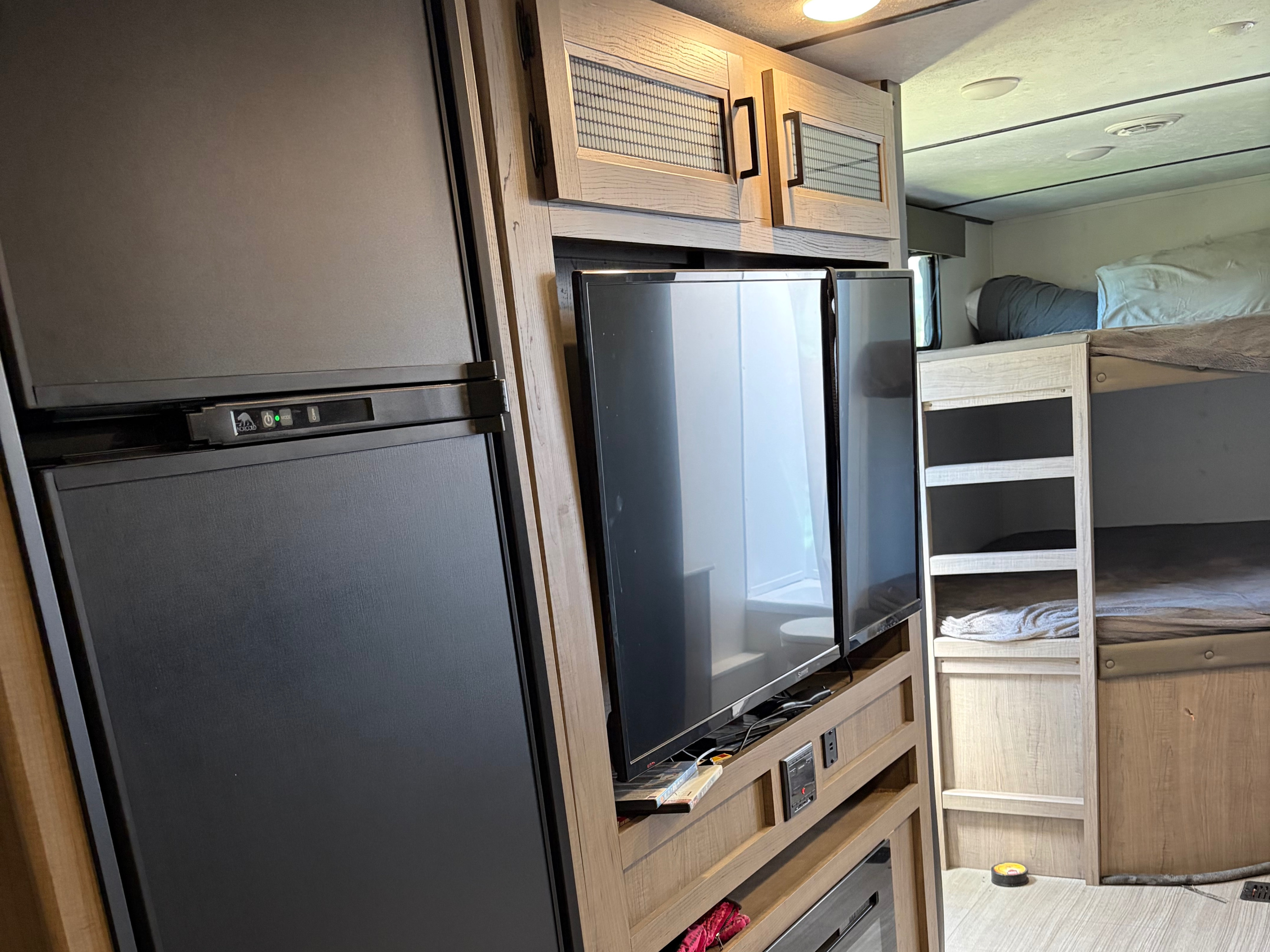 RV rental interior: Features a refrigerator, swing-out TV, bunk beds, and wood-grain cabinets inside a camper.. Keystone RV Hideout 2021