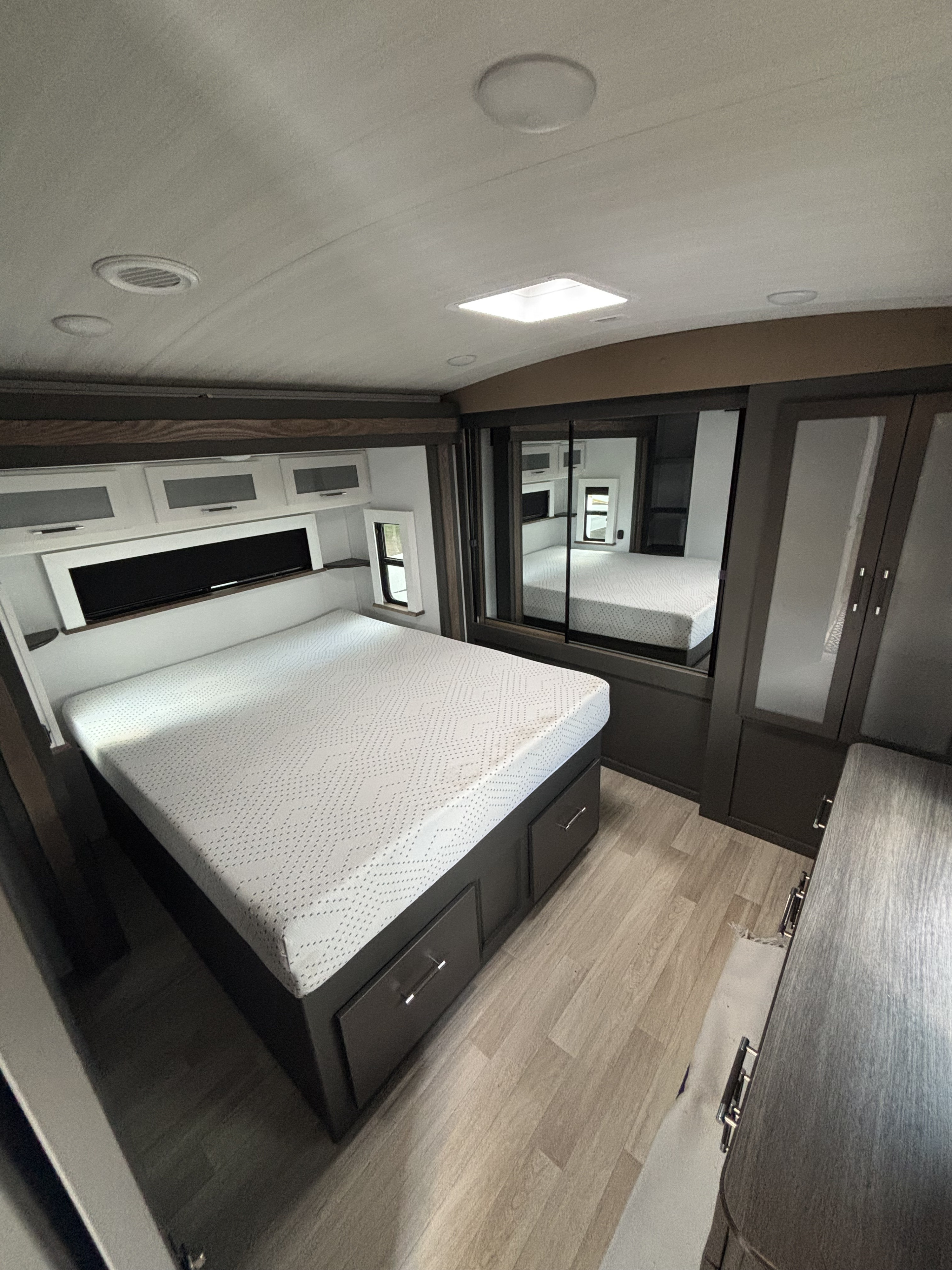 RV rental bedroom showcasing a bed with drawers, mirrored closet doors, and overhead storage. A compact and functional space.. Keystone RV Bullet Premium 2025