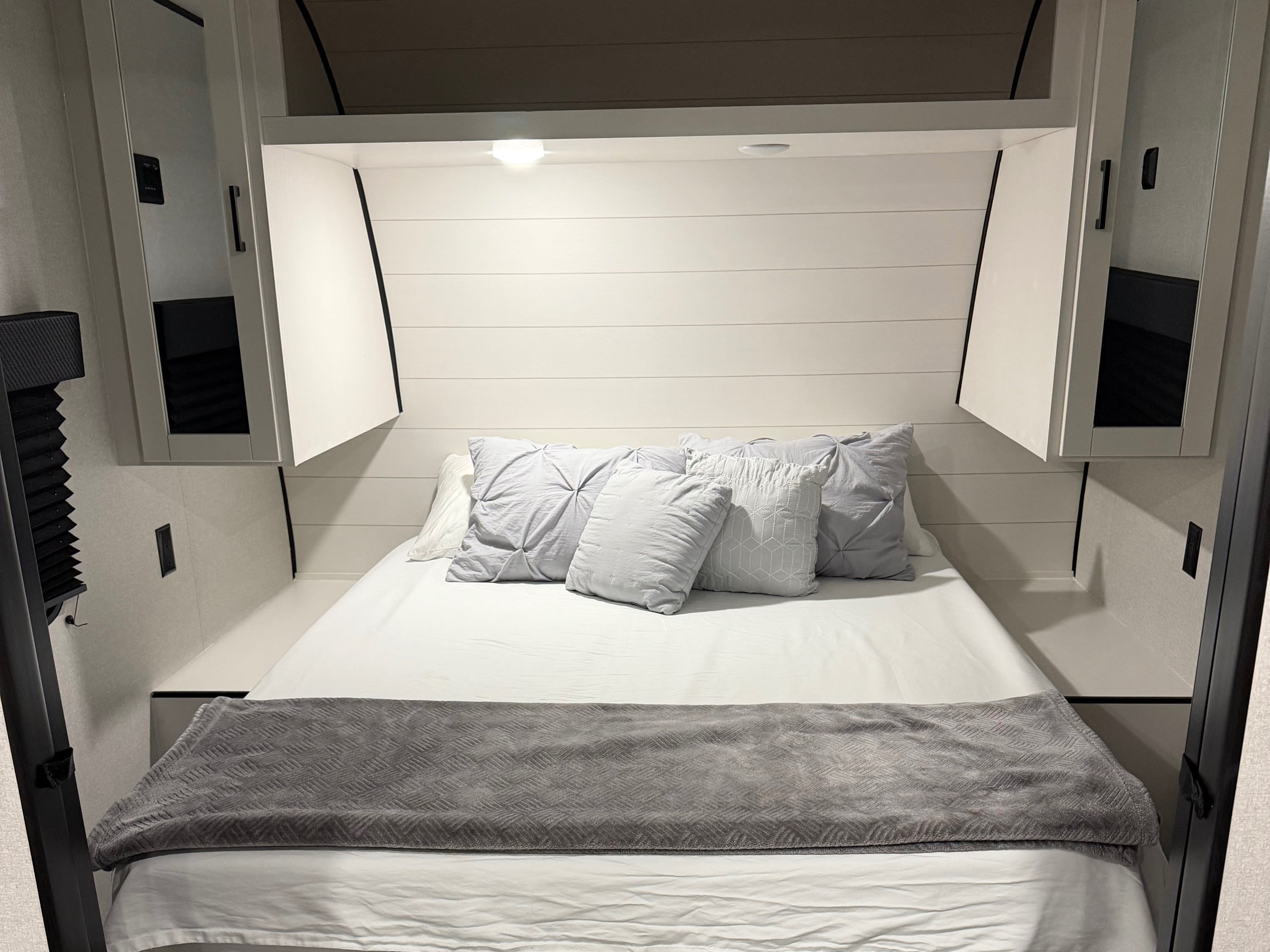 RV rental bedroom with a neatly made bed, white sheets, gray pillows, overhead cabinets, and wood-look flooring. Modern travel trailer interior.. Jayco Jay-flight 2026