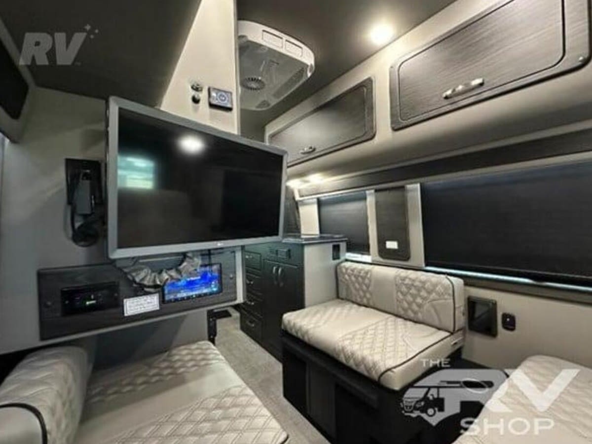RV rental interior: large TV, tech controls, overhead storage, and plush quilted seating for comfortable travel.. Airstream Interstate 2023