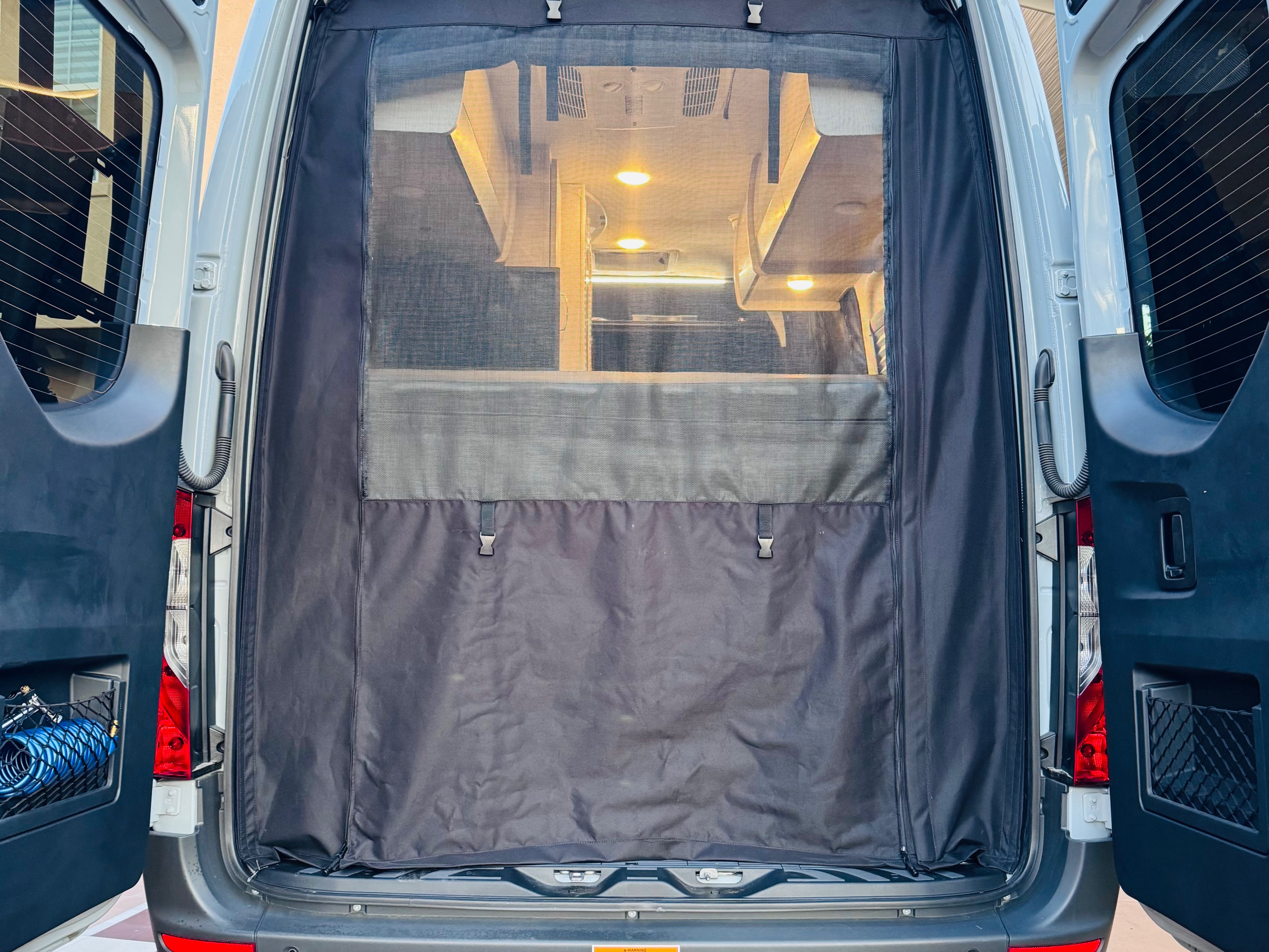RV rental's rear entry, open doors reveal a mesh screen, cozy interior lighting, and practical storage. Adventure awaits.. Thor Tranquility 2025