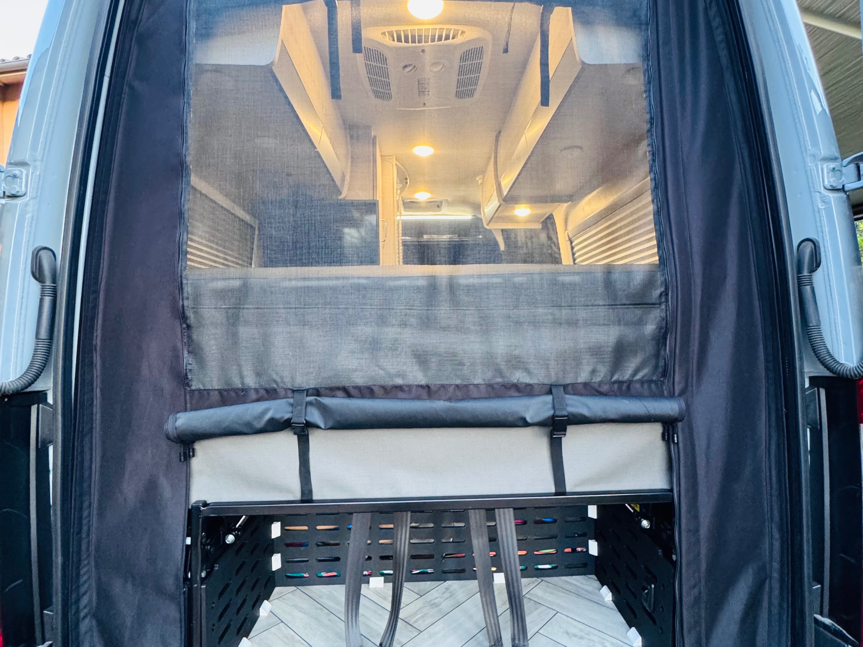RV rental camper van rear: Mesh screen, bed, overhead lights, and lower storage rack visible from outside.. Thor Tranquility 2025