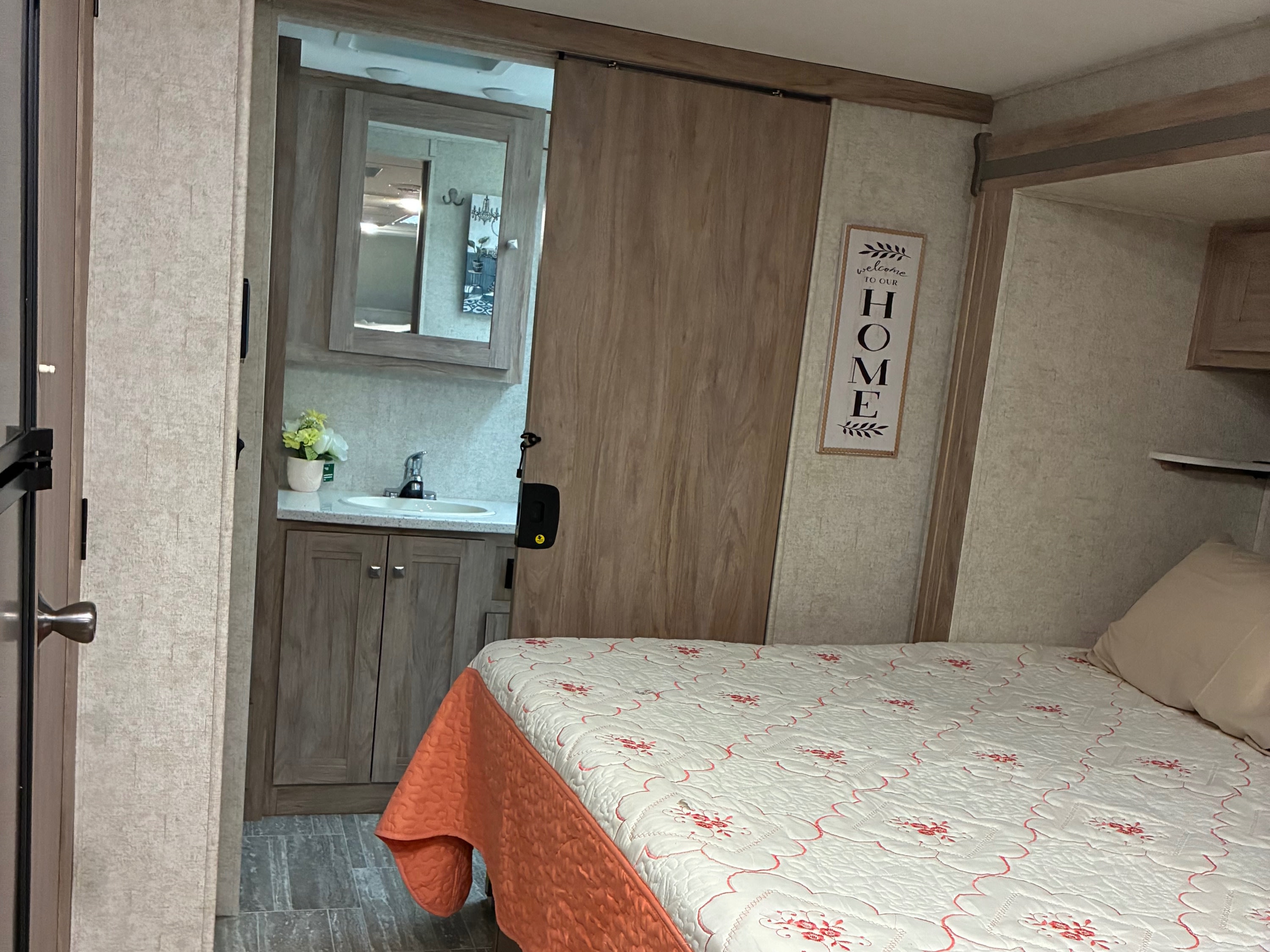 This RV rental features a cozy bedroom with a quilted bed, a vanity area visible through a sliding barn door, and tiled floors.. Forest River Forester 2020
