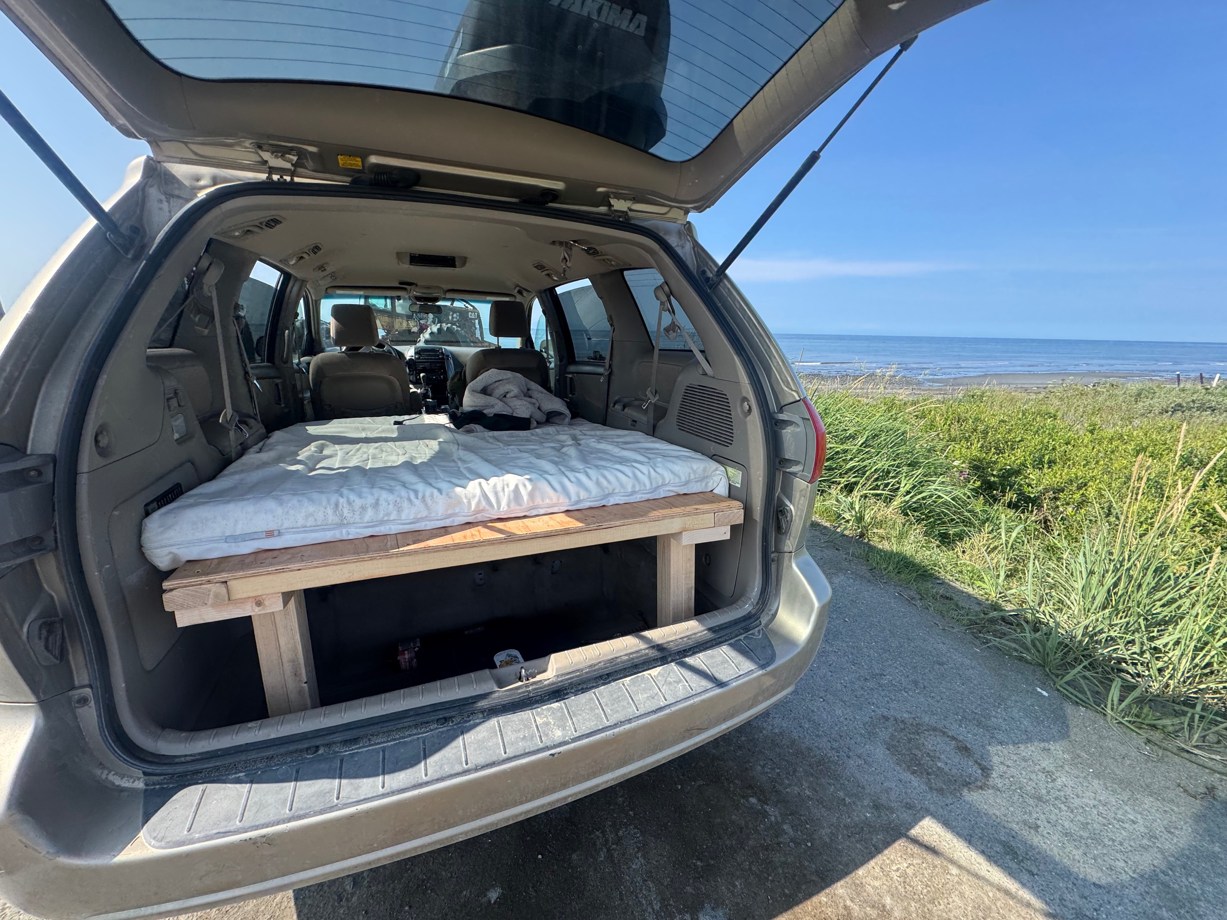 Minivan with a DIY bed platform for an RV rental adventure, offering a cozy sleep space and scenic ocean view.. Toyota Sienna 2009