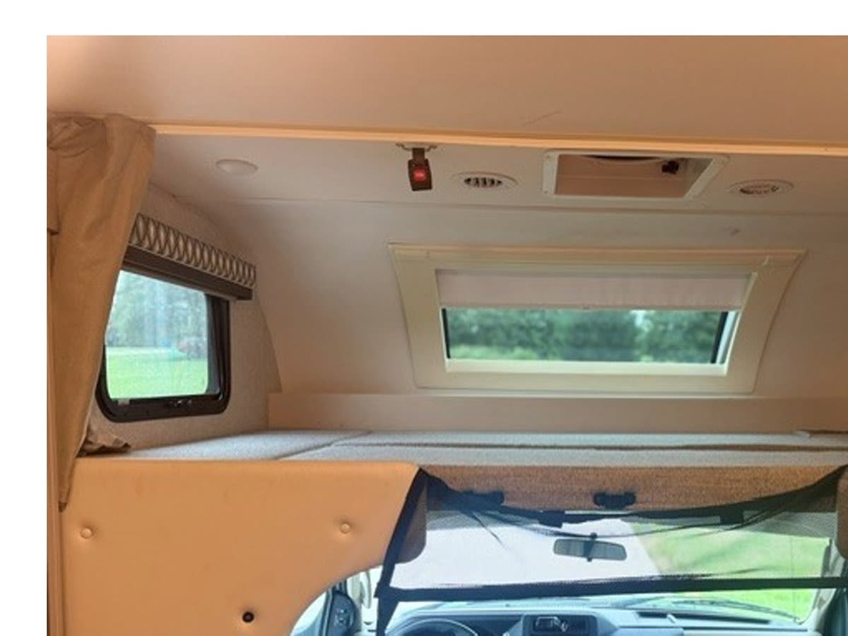 Explore this RV rental's cozy over-cab bunk bed, front windows, and spacious interior cabin area, perfect for travel.. Thor Quantum 2023