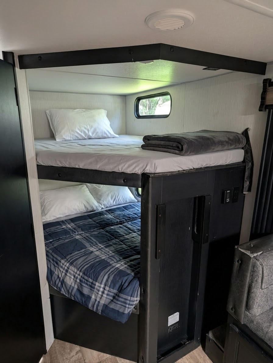 This RV rental features stacked bunk beds, with a window view from the top and a cozy plaid blanket on the lower.. Forest River Cherokee Grey Wolf 2022