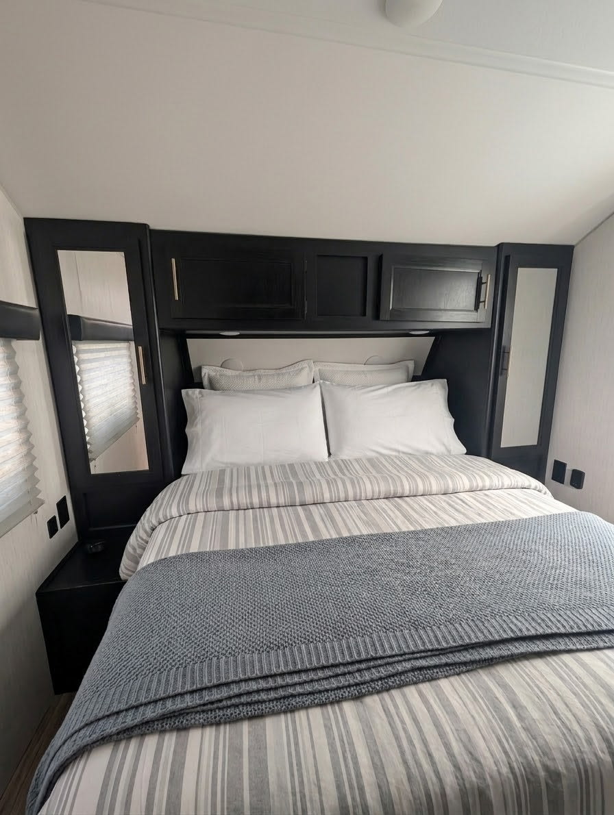 Cozy RV rental bedroom featuring a modern black headboard with storage, striped bedding, and a comfy gray throw blanket.. Forest River Cherokee Grey Wolf 2022