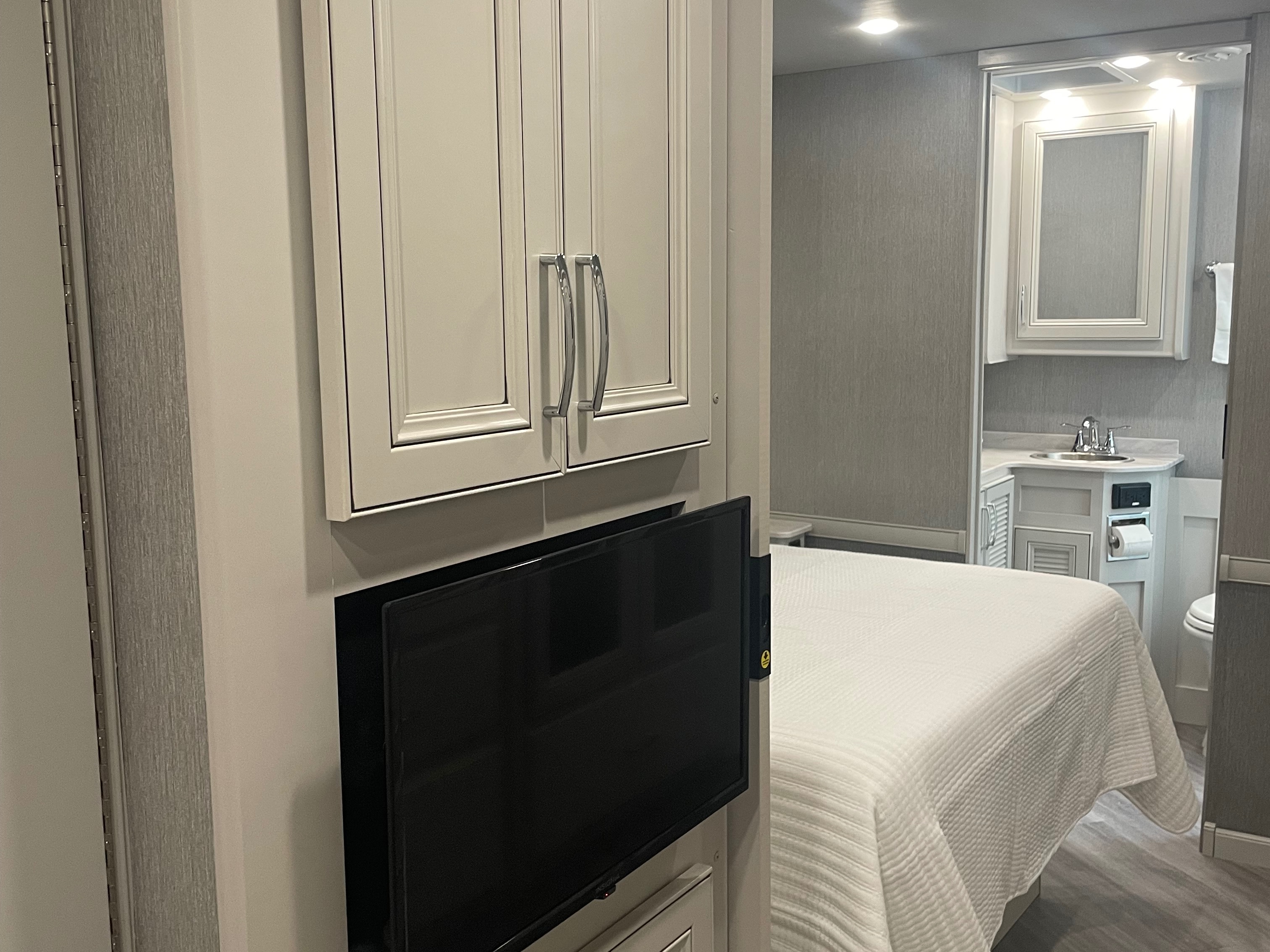 RV rental bedroom with a white bed, built-in TV, and an attached bathroom with a sink and toilet. Cozy accommodations.. Holiday Rambler Vacationer 2022