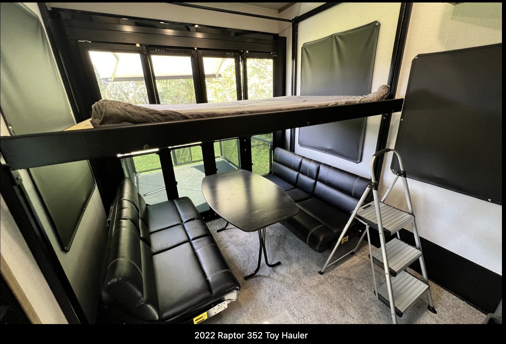 Spacious toy hauler rv rental interior features a bunk bed, dinette, and large windows revealing green outdoors.. Keystone RV Raptor Toy Hauler 2022