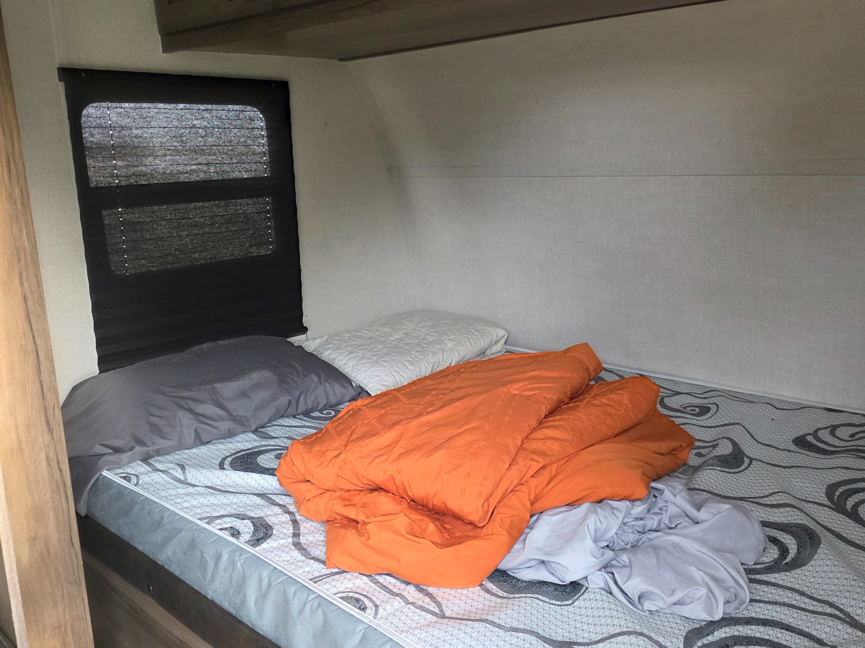 Cozy RV rental bedroom with a bed, orange comforter, pillows, and window blinds.. Avenger LT 2021