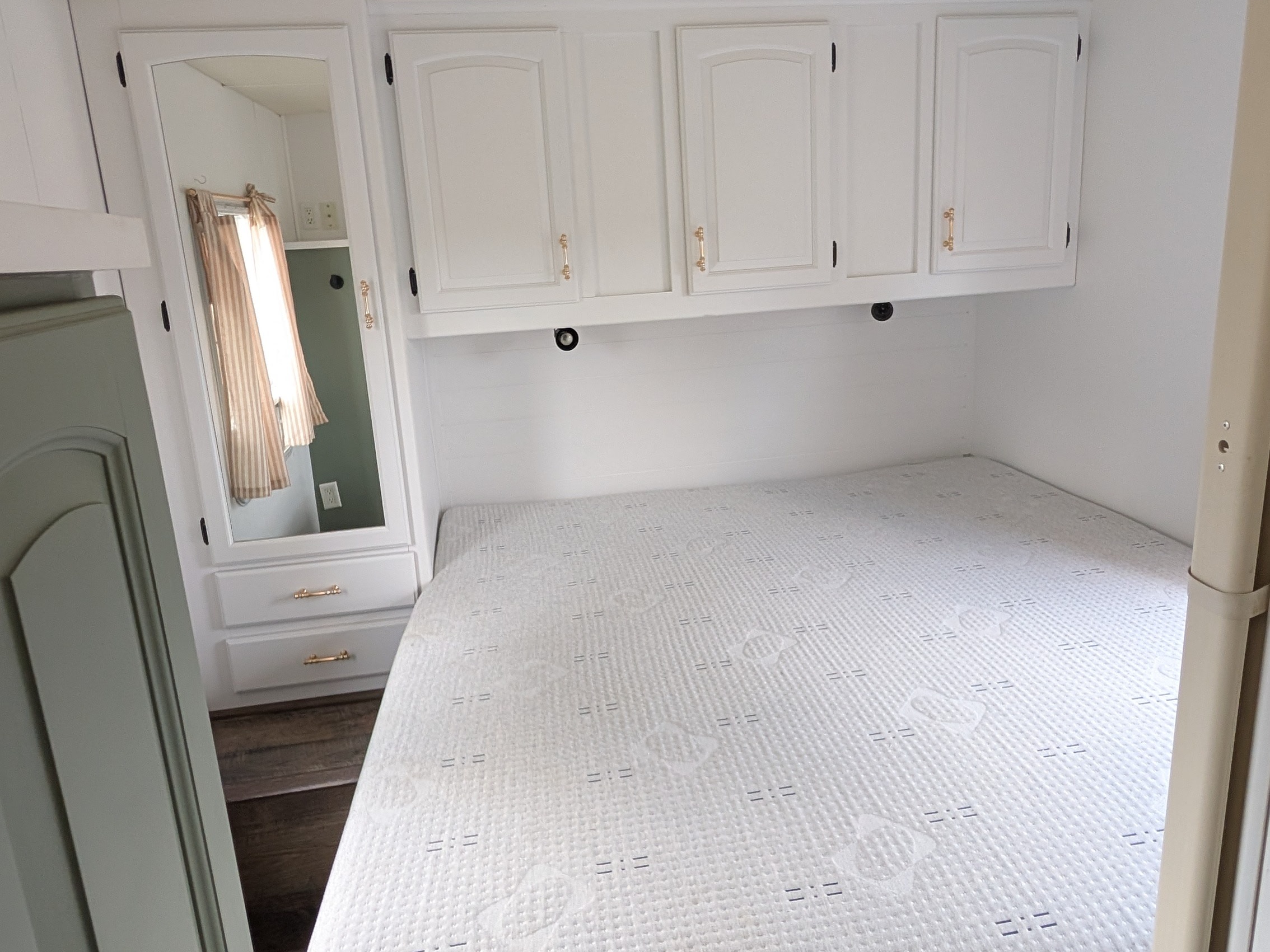 Bright and tidy RV rental bedroom showcasing a bed, white overhead cabinets, and a reflective mirror. Ready for your journey!. Jayco Greyhawk 2007