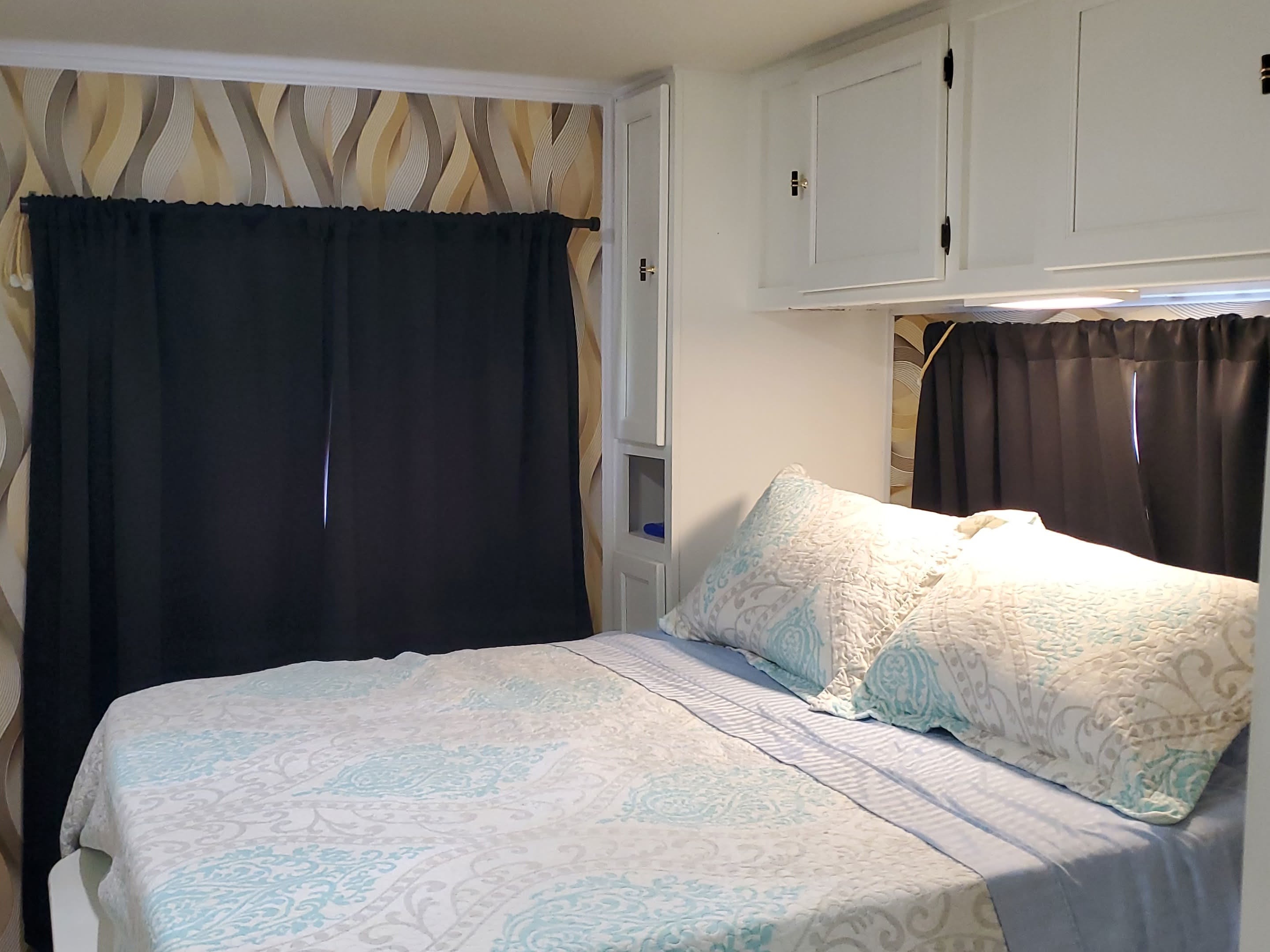 Cozy RV rental bedroom featuring patterned wallpaper, dark curtains, and practical overhead cabinets for a comfortable stay.. CoachMen Freelander 2012