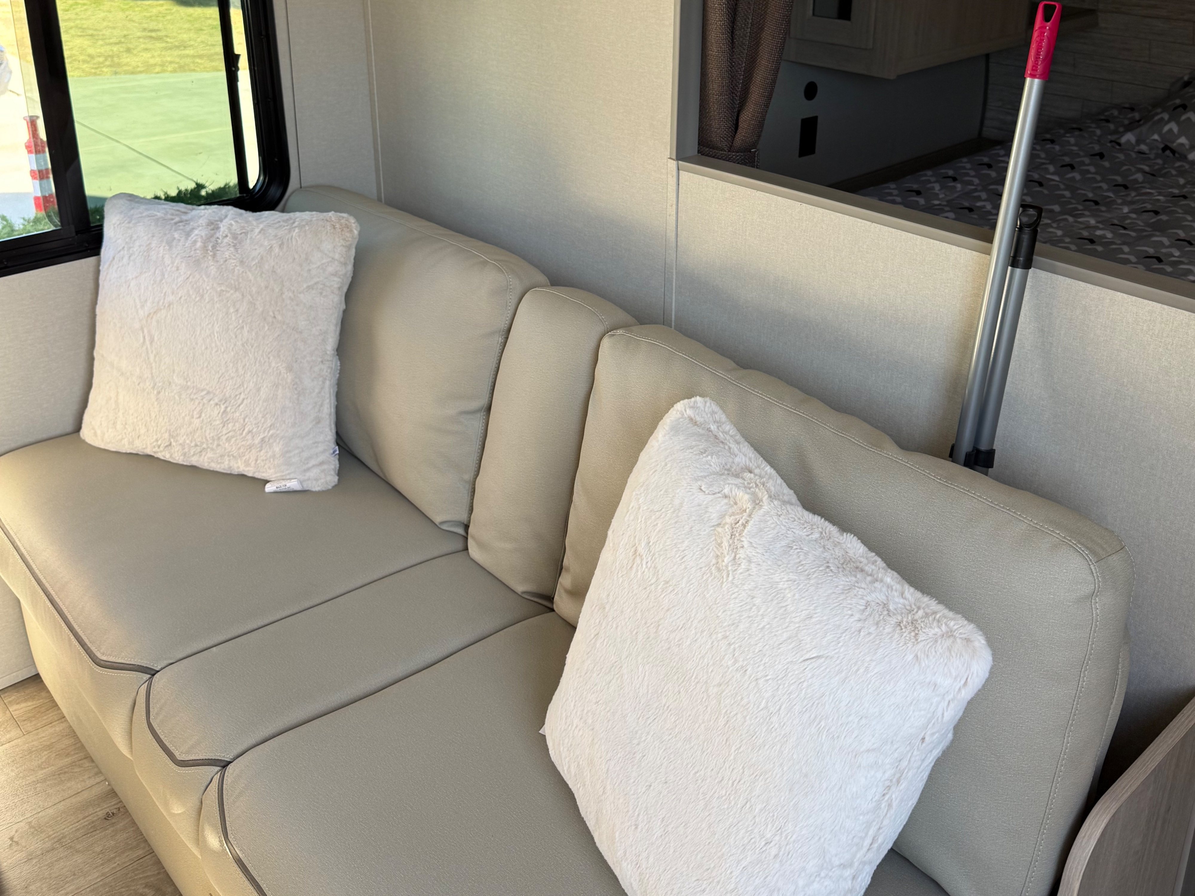 RV rental living space: Light-colored sofa with fluffy white cushions, a window, and view of the bed area.. Coachmen Catalina 261 bh 2026