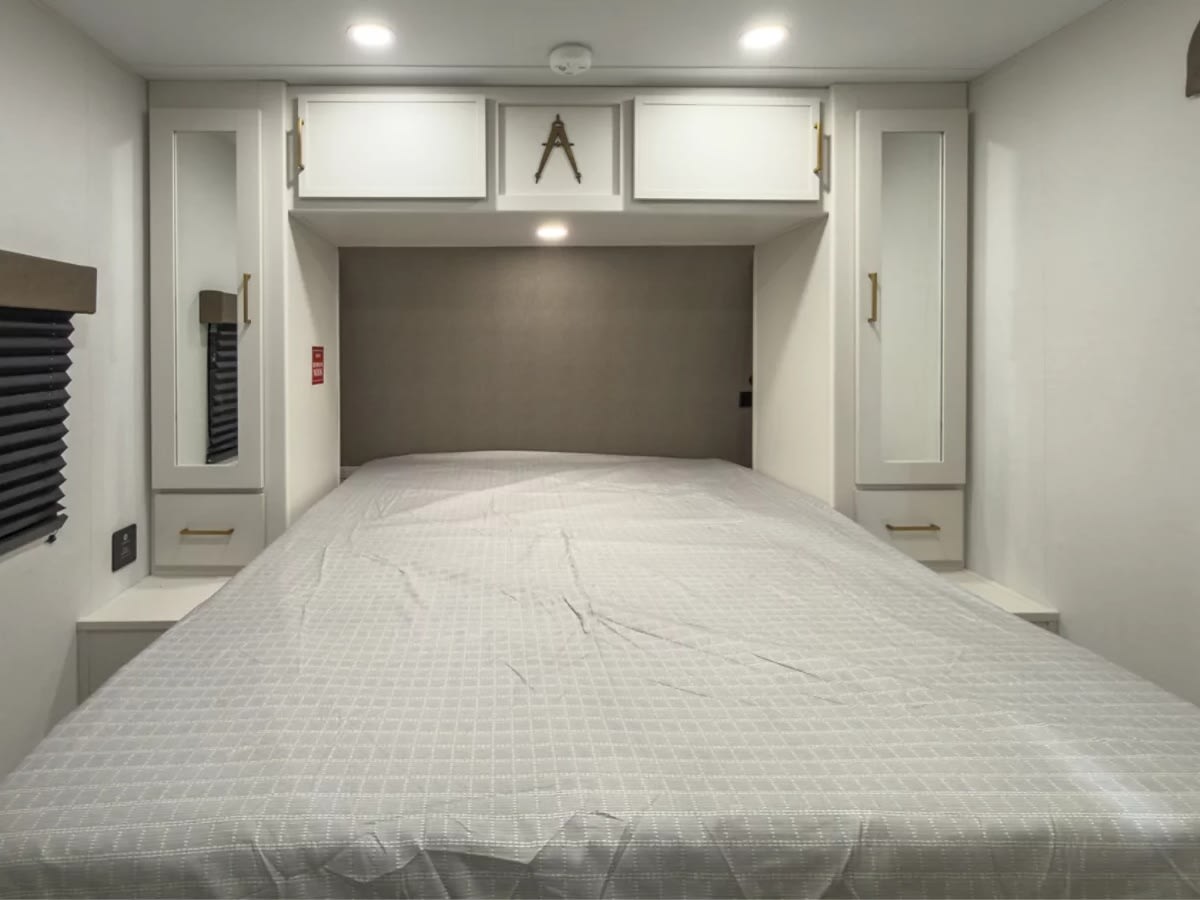 Modern RV rental bedroom, featuring a large bed, mirrored closets, and overhead storage for comfortable travel.. Grand Design Transcend 2027