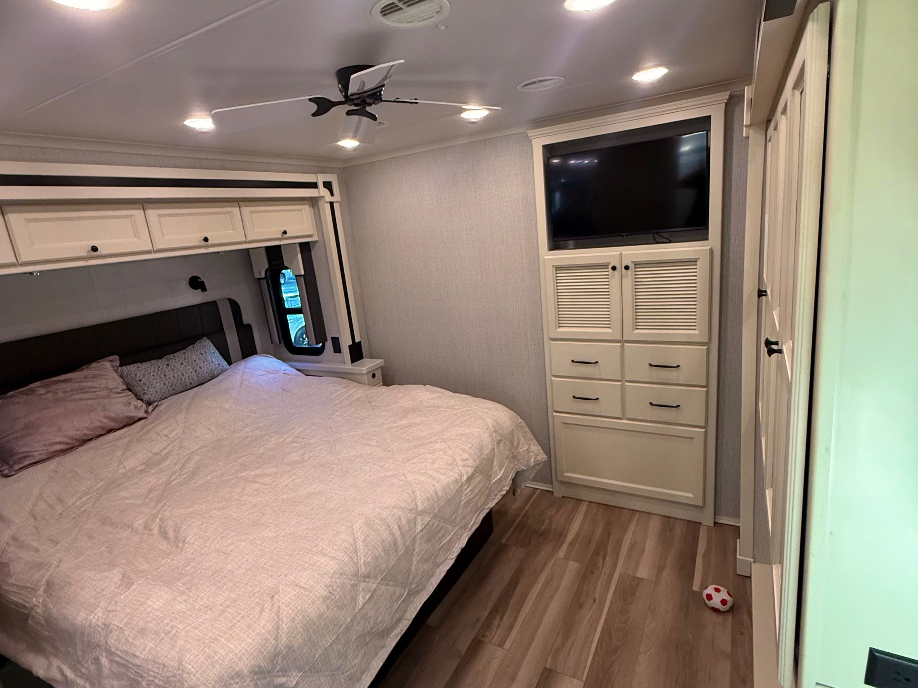 Light-filled RV rental bedroom shows a bed, overhead cabinets, a TV unit, and ceiling fan over wood-look flooring.. Allegro Allegro Open Road 2026
