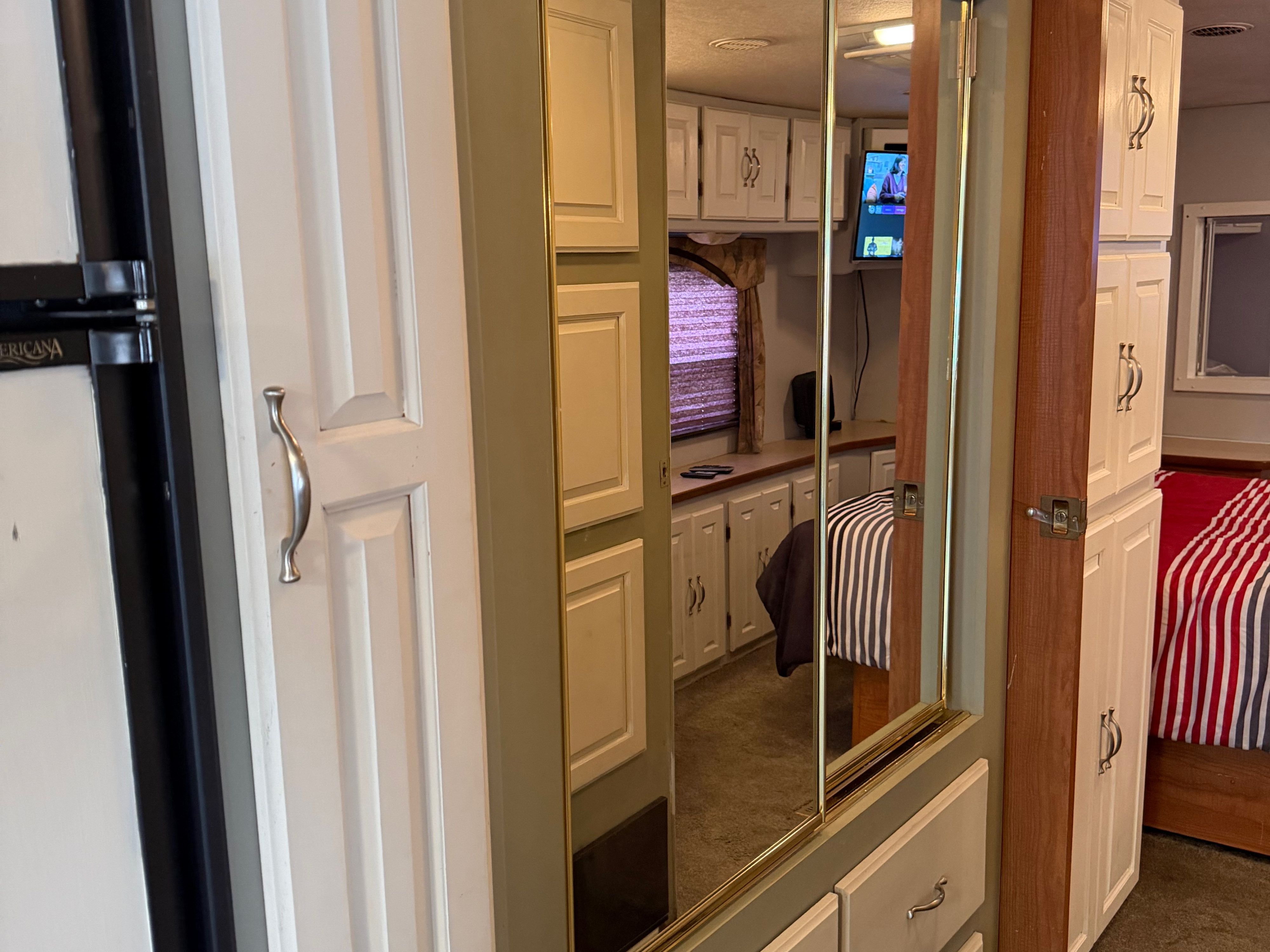 Cozy RV rental interior: a fridge on the left, mirrored closet reflecting a TV and bed, and white cabinets on the right.. Coachmen Cross Country 2003
