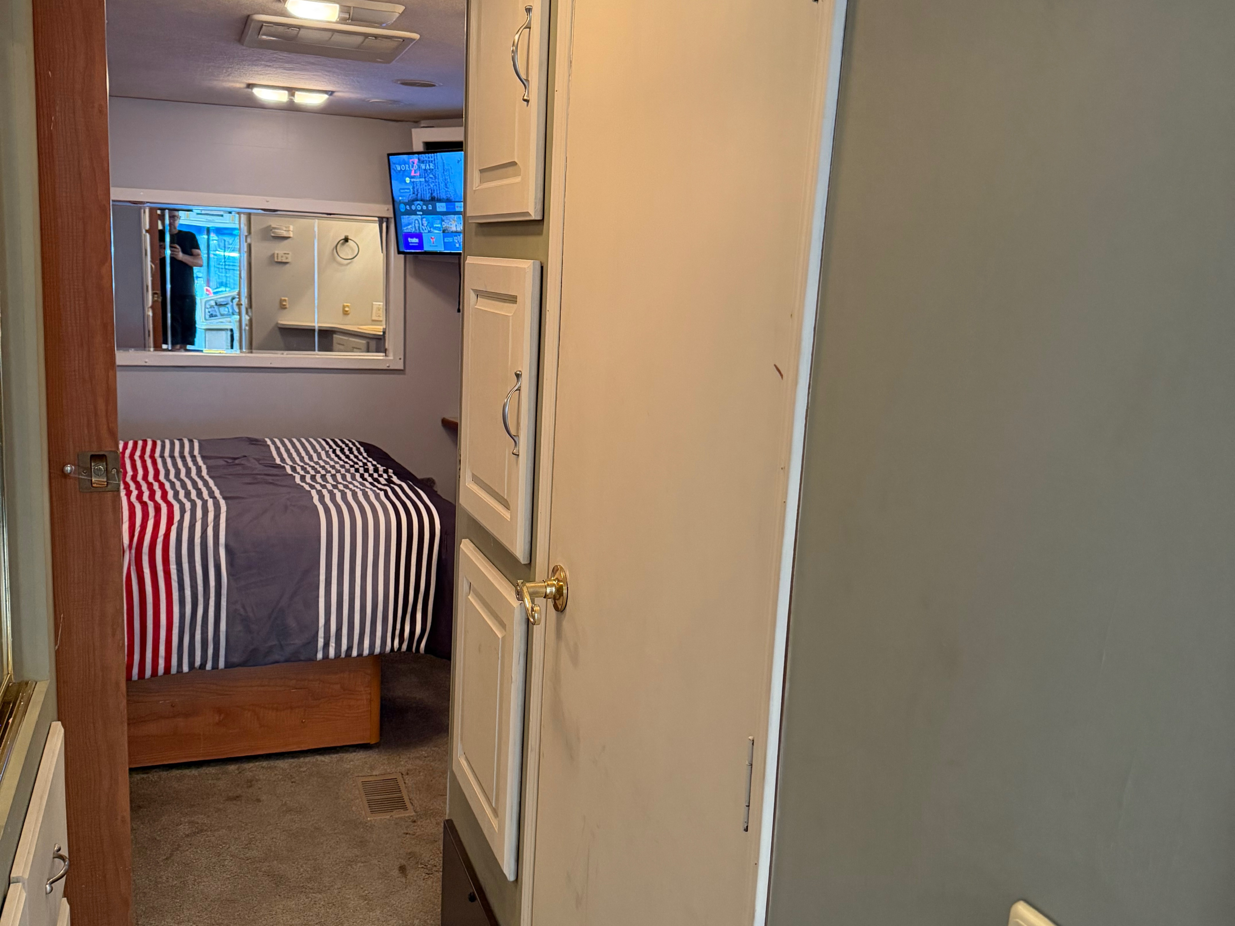 RV rental bedroom: a cozy space with a striped bed, wall-mounted TV, and built-in cabinets, perfect for your journey.. Coachmen Cross Country 2003