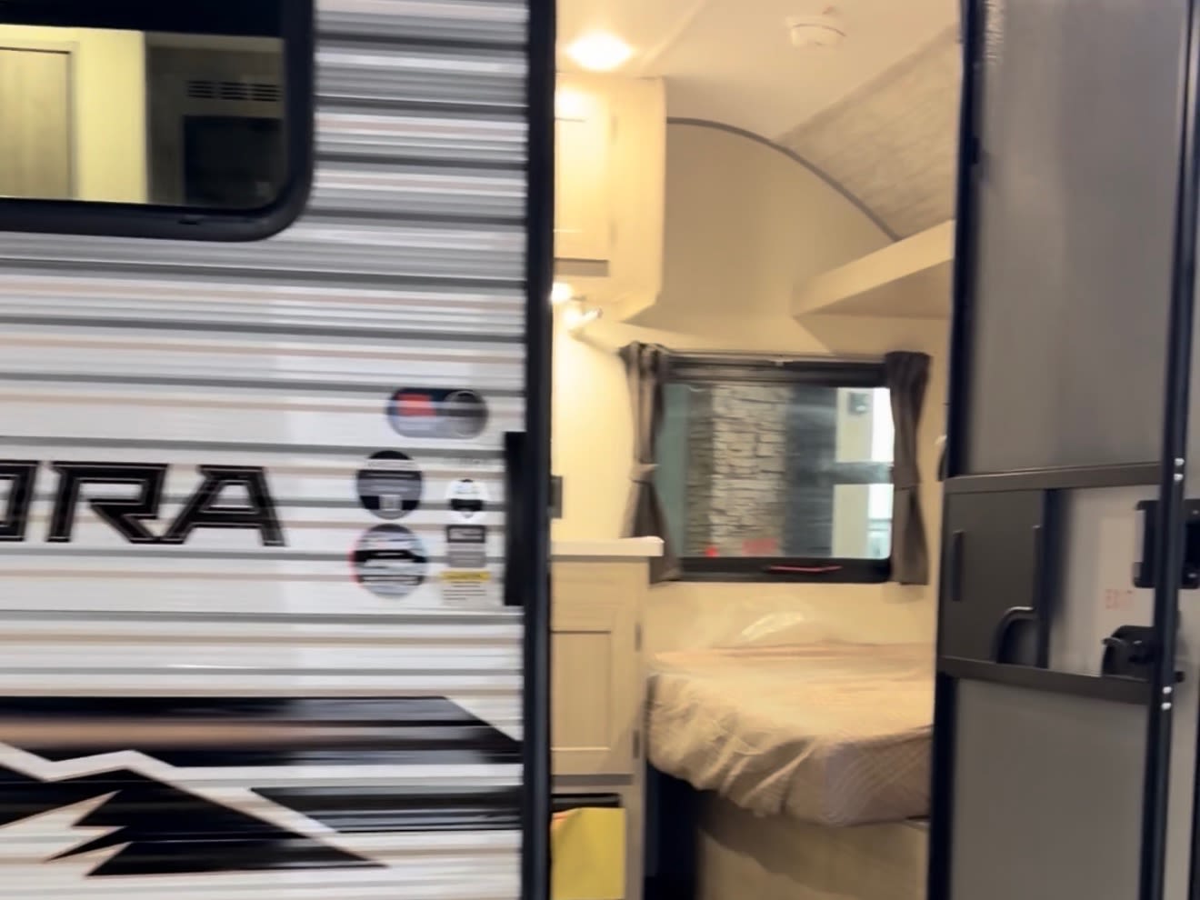 View of a compact RV rental. The bedroom with a bed and window is seen through the open door, alongside the striped exterior.. Forest River Aurora Aurora Light 2026