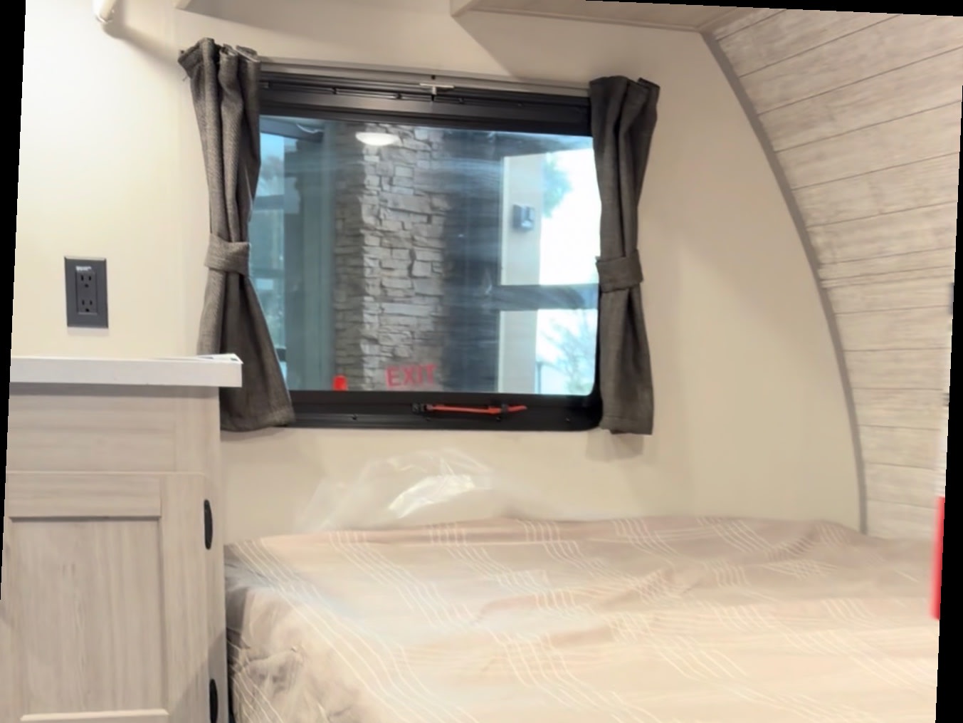 RV rental interior: A cozy bedroom with a window, grey curtains, light wood cabinet, outlet, and patterned bed.. Forest River Aurora Aurora Light 2026