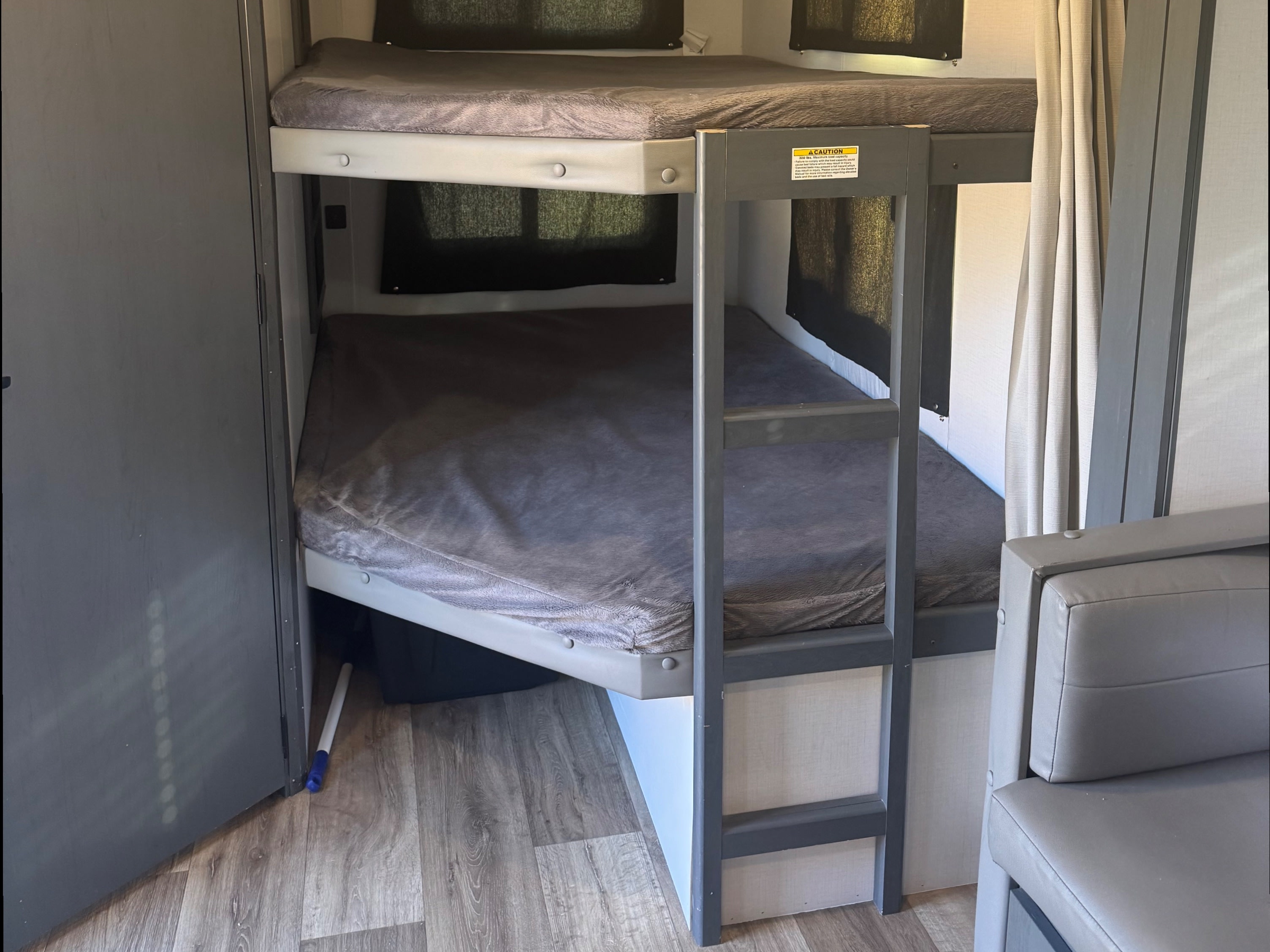 Inside an rv rental, spacious bunk beds with grey bedding, dark window blinds, and a built-in ladder for comfortable sleep.. Keystone RV Bullet Ultra Lite 2022