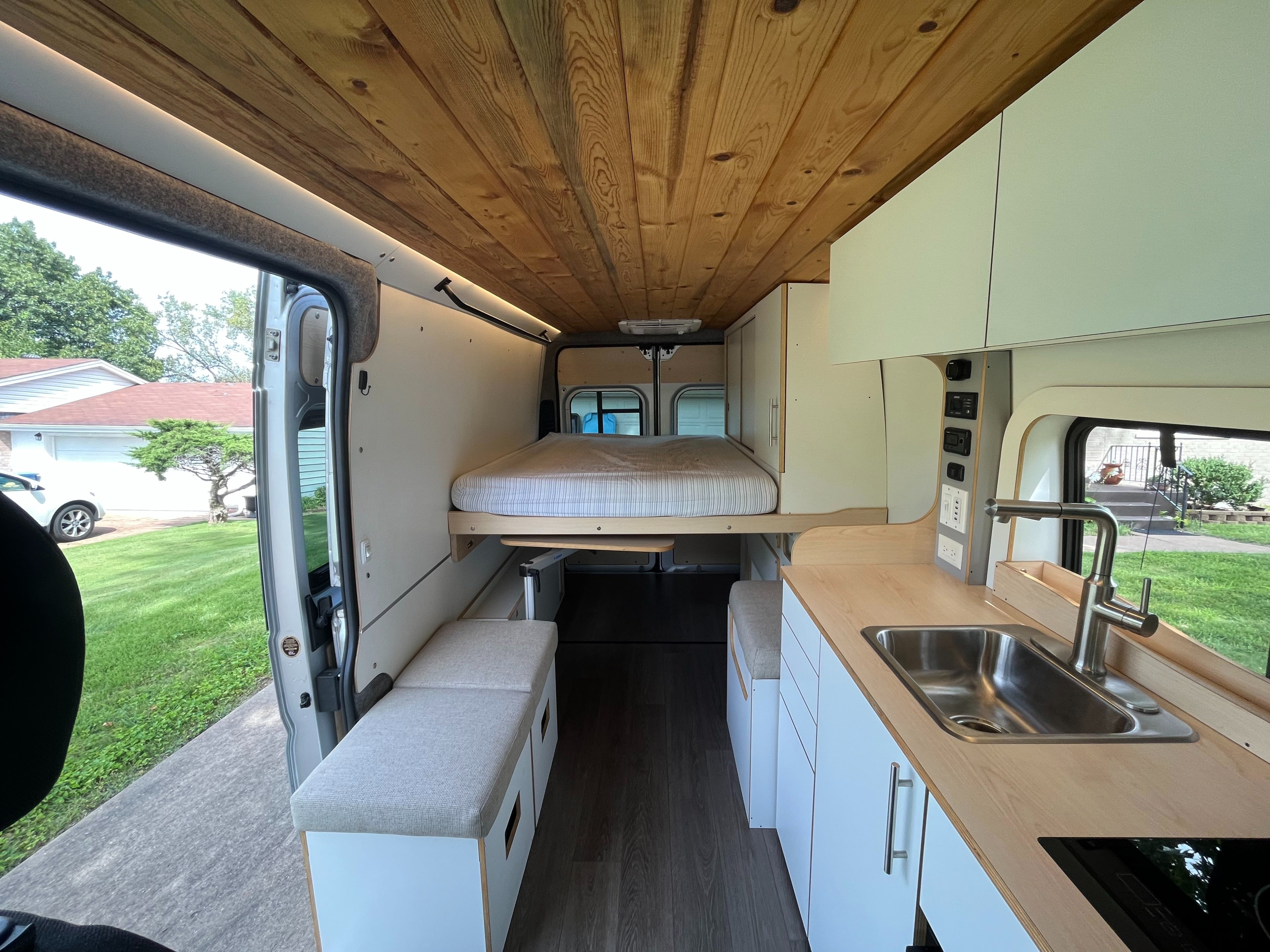 Inside a stylish rv rental: wood ceiling, bed, kitchen, and bench seating in a custom camper van.. Dave & Matt Vans Dave & Matt Vans Class B 2023