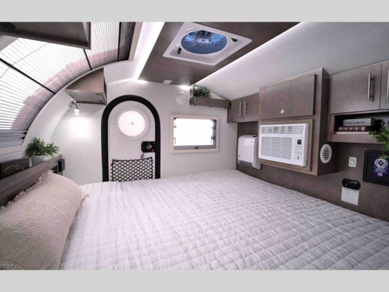 Cozy RV rental interior featuring a comfortable bed, AC unit, overhead storage, and a unique arched door.. nuCamp T@G 2024