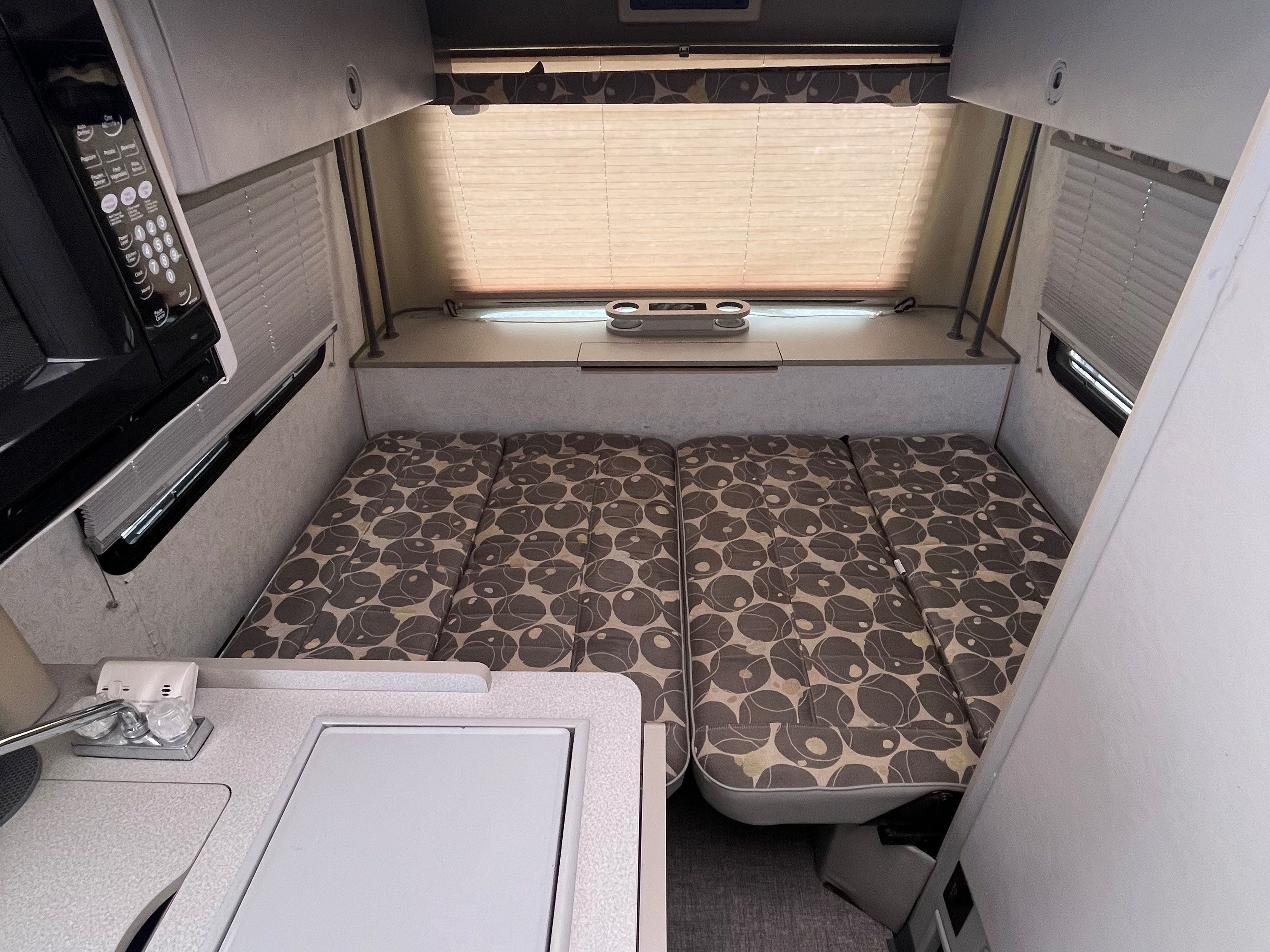 Cozy RV rental interior featuring a bed/dinette with patterned cushions, a compact kitchen with microwave, and window blinds.. Eurovan Camper Eurovan Camper Class B 2003