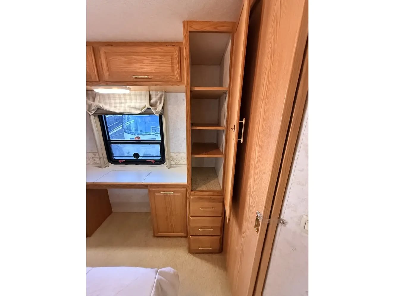 RV rental interior featuring a wooden desk, window with an "EXIT" sign outside, and built-in storage shelves, drawers, and cabinets.. Winnebago Adventurer 2003