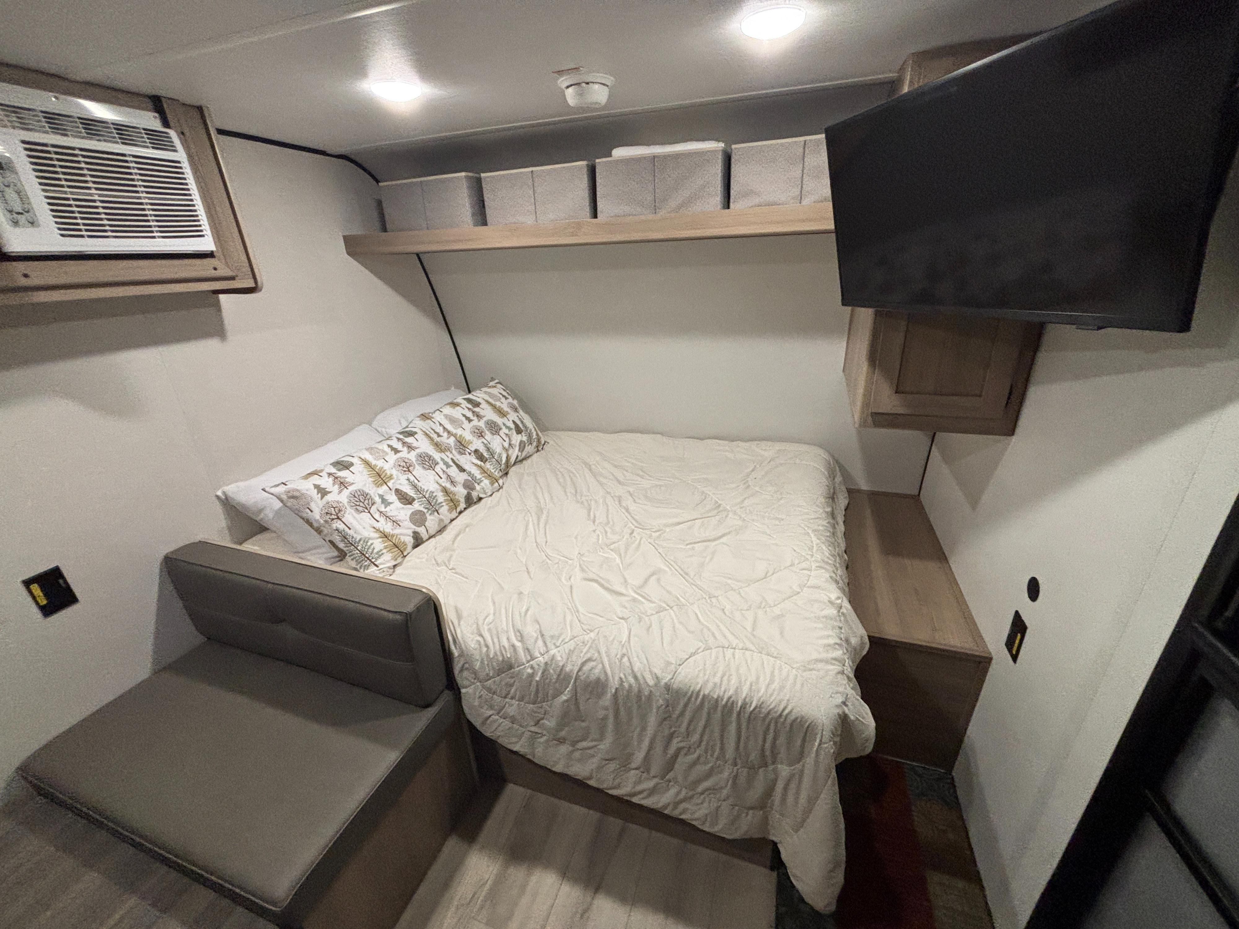 RV rental sleeping area features a cozy bed, seating, AC, TV, and overhead bins.. Keystone RV Coleman 2025
