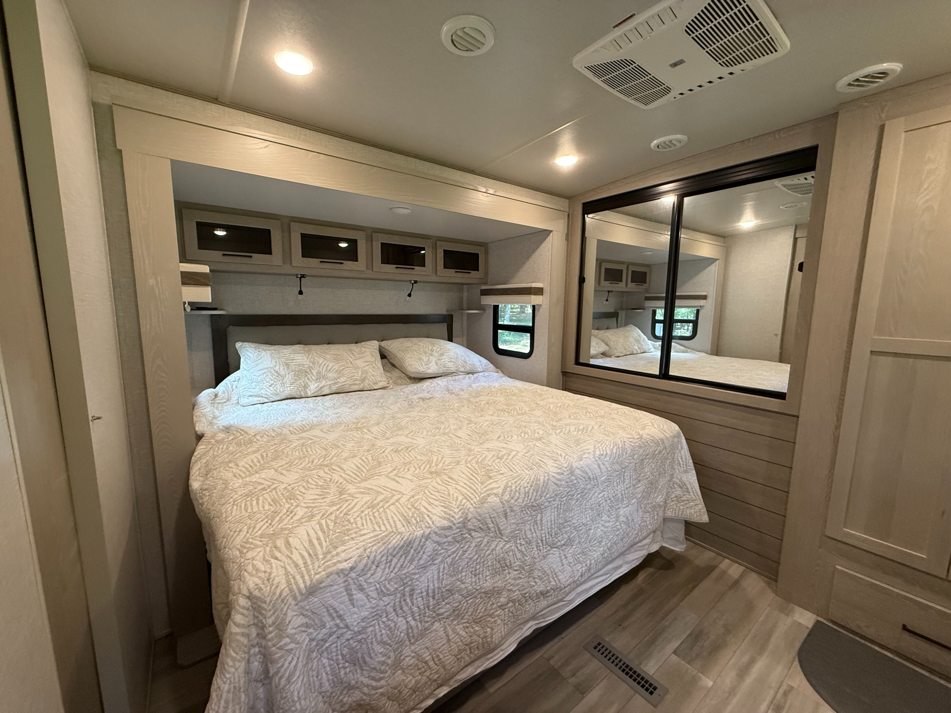 Spacious RV rental bedroom featuring a queen bed with leaf-patterned bedding, overhead storage, and a mirrored closet.. Forest River Rockwood Signature 2023