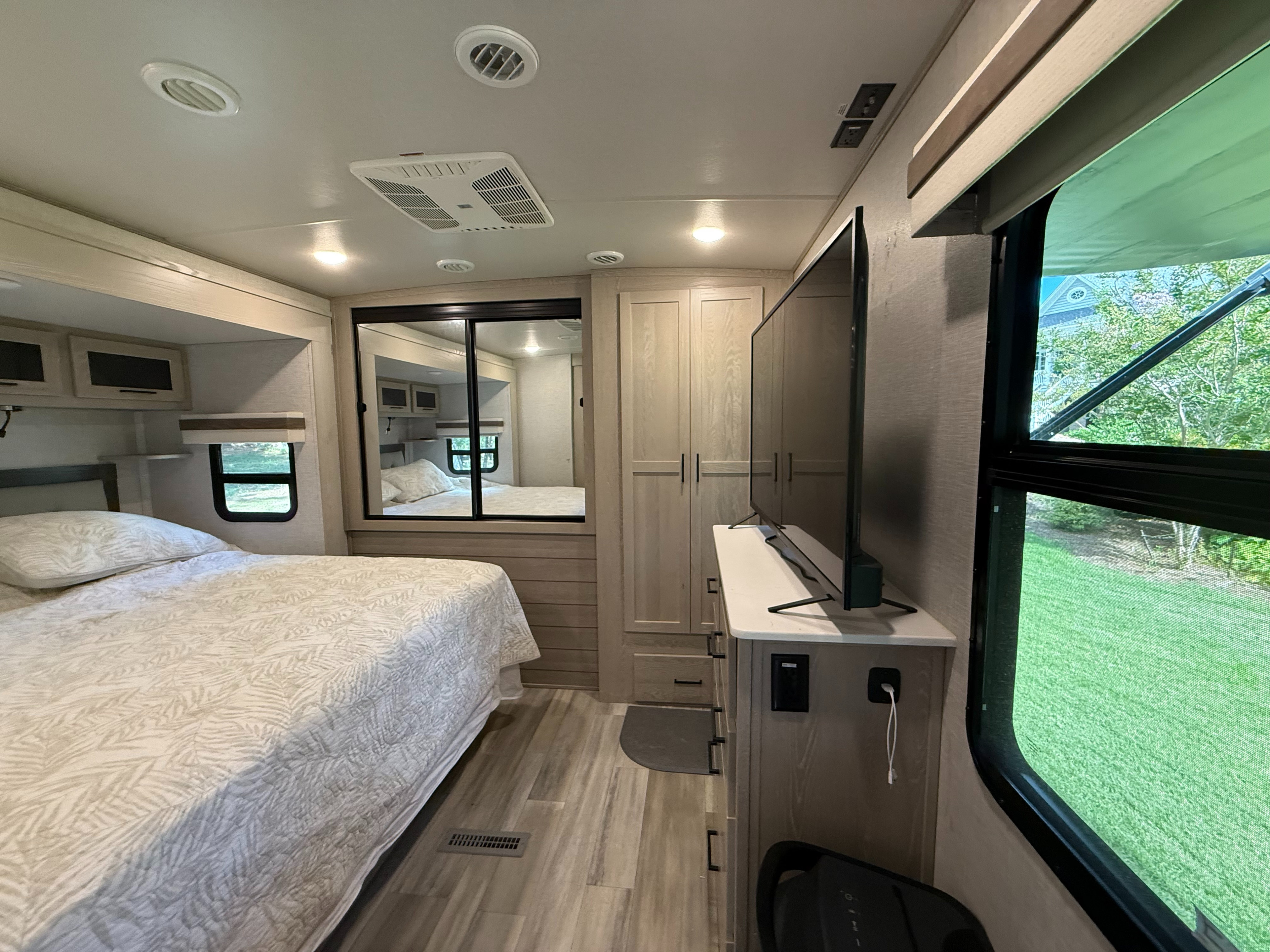 Cozy RV rental bedroom with a comfortable bed, mirrored closet, TV, and large windows offering scenic outdoor views.. Forest River Rockwood Signature 2023