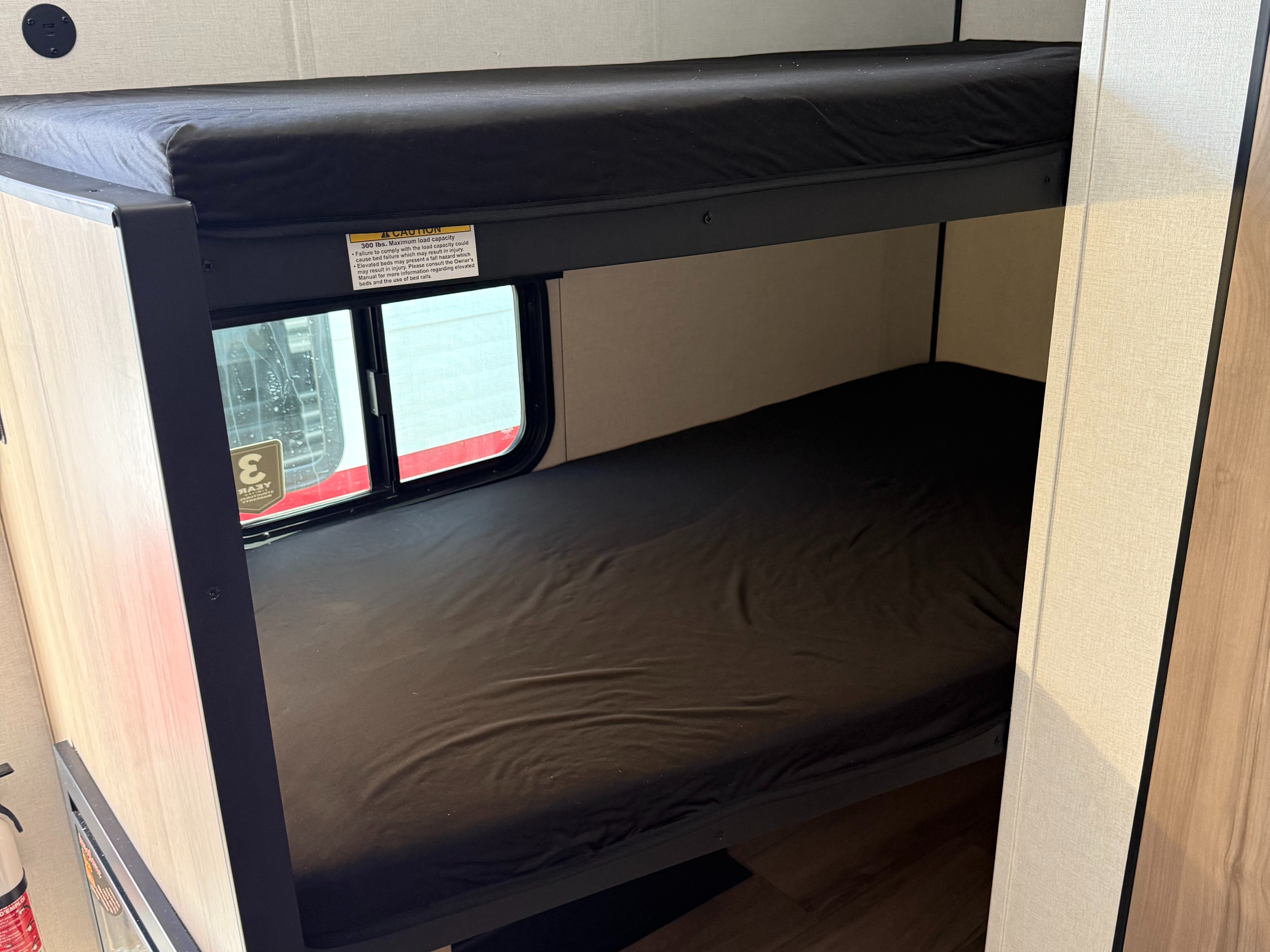 RV rental: Stacked bunk beds with dark mattresses. The top bunk has a 300 lbs warning label; a window is by the lower bed.. Keystone RV Coleman 2026