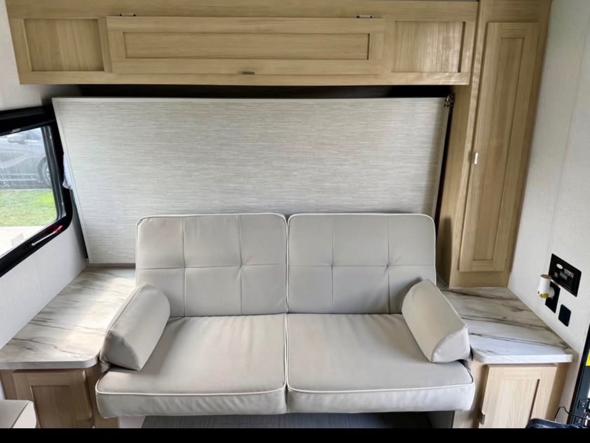 Modern RV rental interior: light-colored convertible sofa, overhead cabinets, and practical countertops maximize space for travel.. Forest River Wildwood FSX 2023