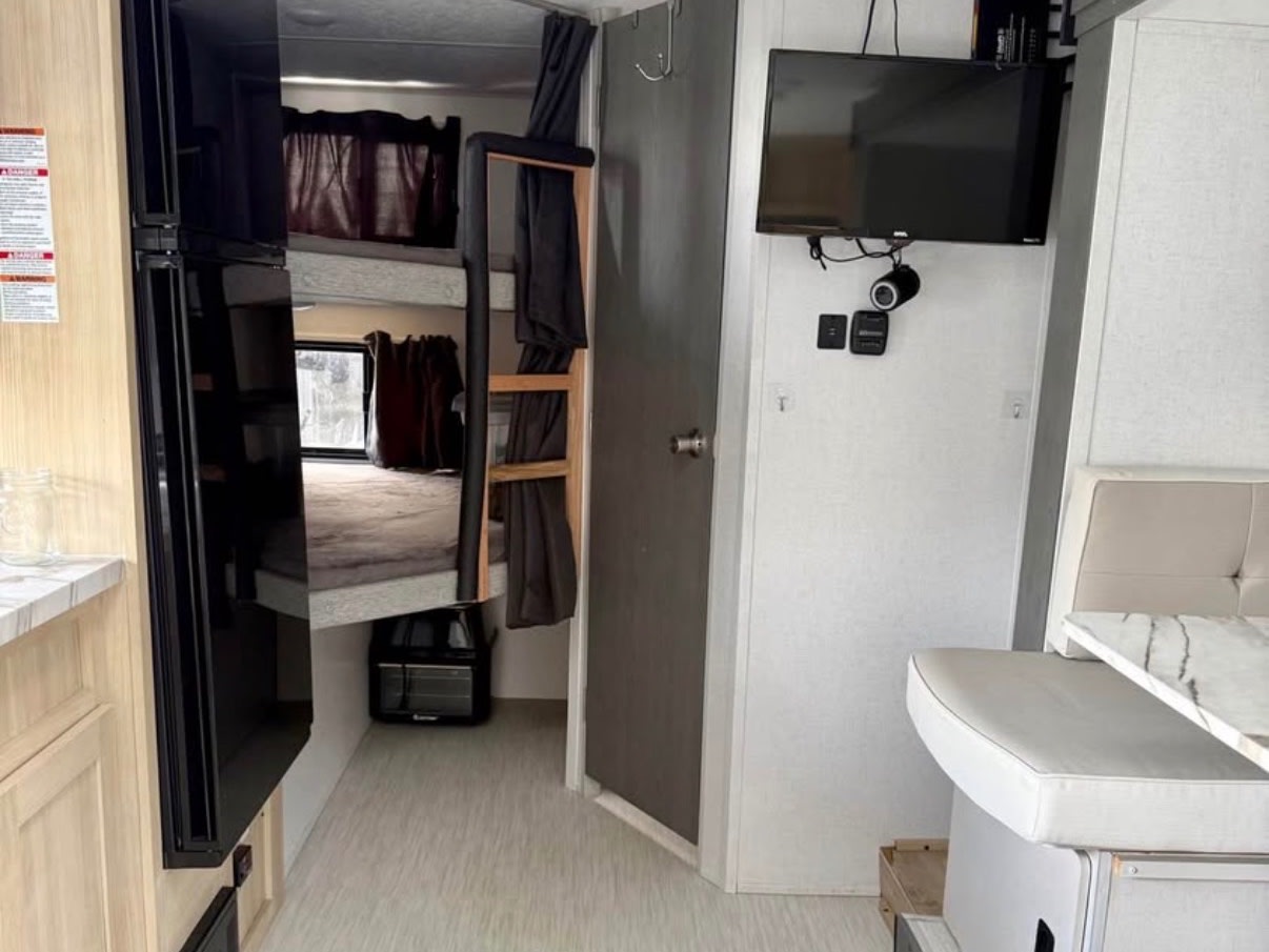 Inside an RV rental, featuring bunk beds, a dining booth, kitchen area, and wall-mounted TV. A compact, functional living space.. Forest River Wildwood FSX 2023