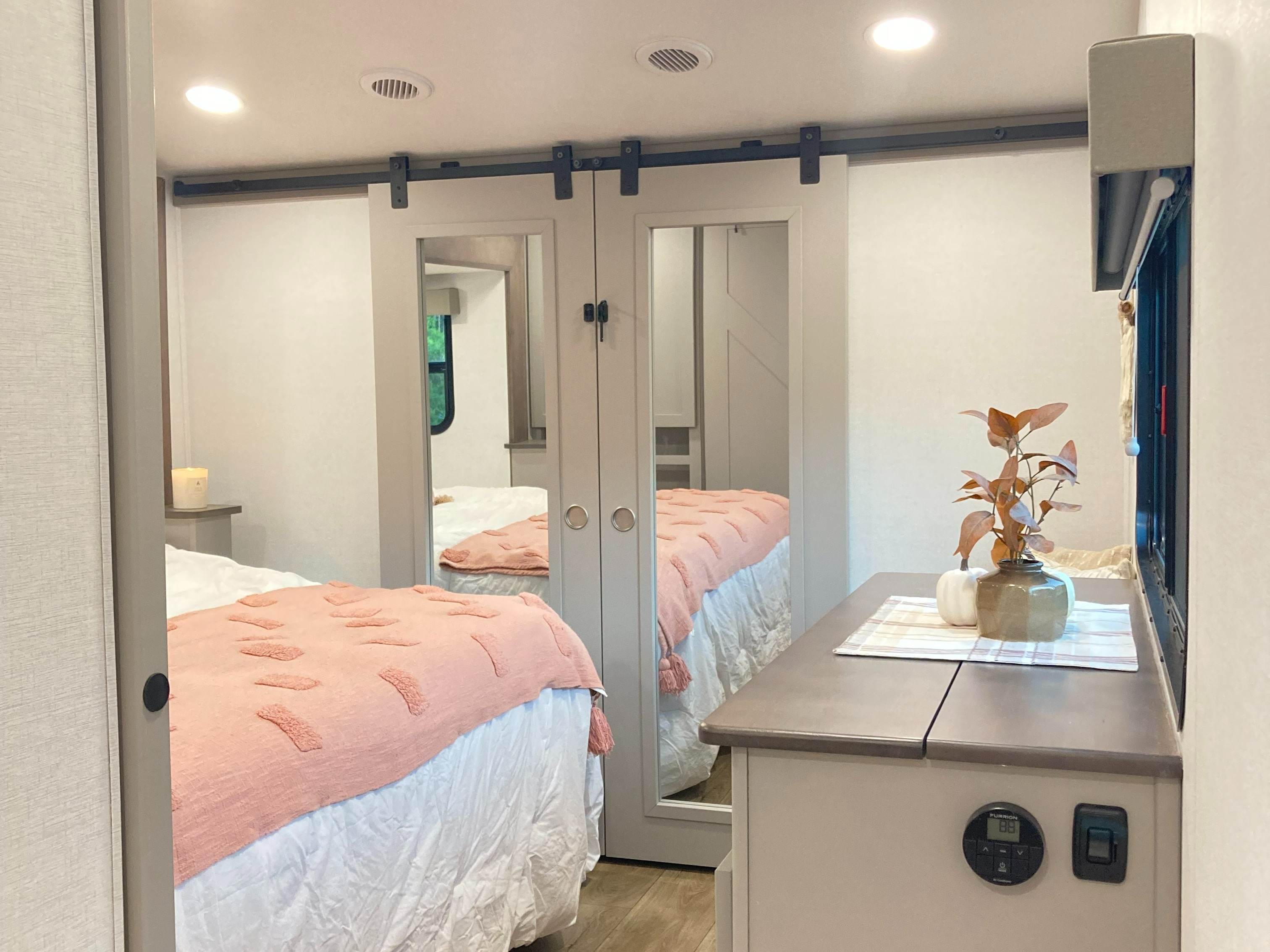 Modern RV rental bedroom boasts mirrored sliding doors, a plush bed with pink accents, and smart controls.. Alliance RV Avenue 2026