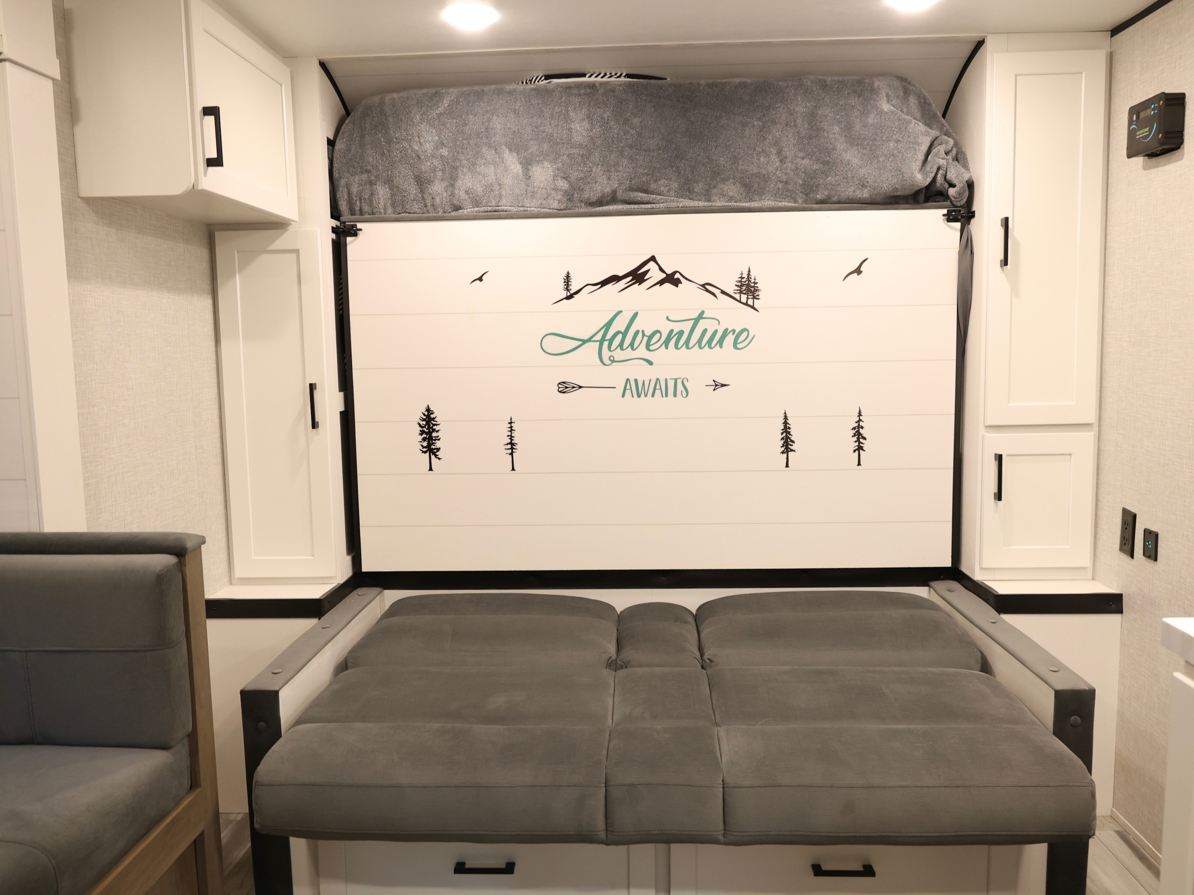 RV rental interior features a cozy convertible bed with "Adventure Awaits" wall art, overhead storage, and white cabinets.. Jayco Jay Flight SLX Baja Edition 2025