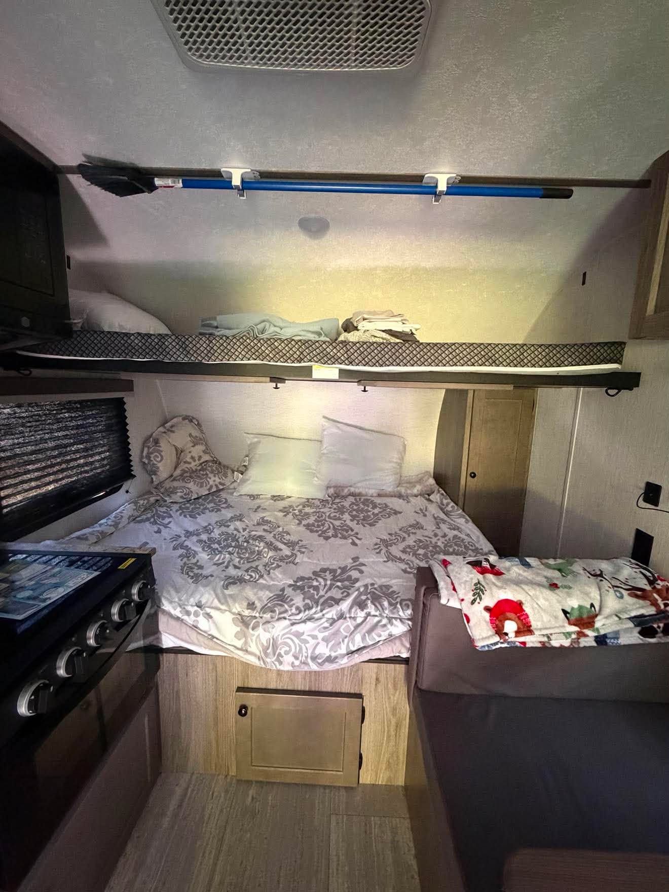 RV rental interior showcasing a comfortable main bed, upper bunk bed, kitchen area with stove, and sofa seating.. Sunset Park RV Sun Lite 2025