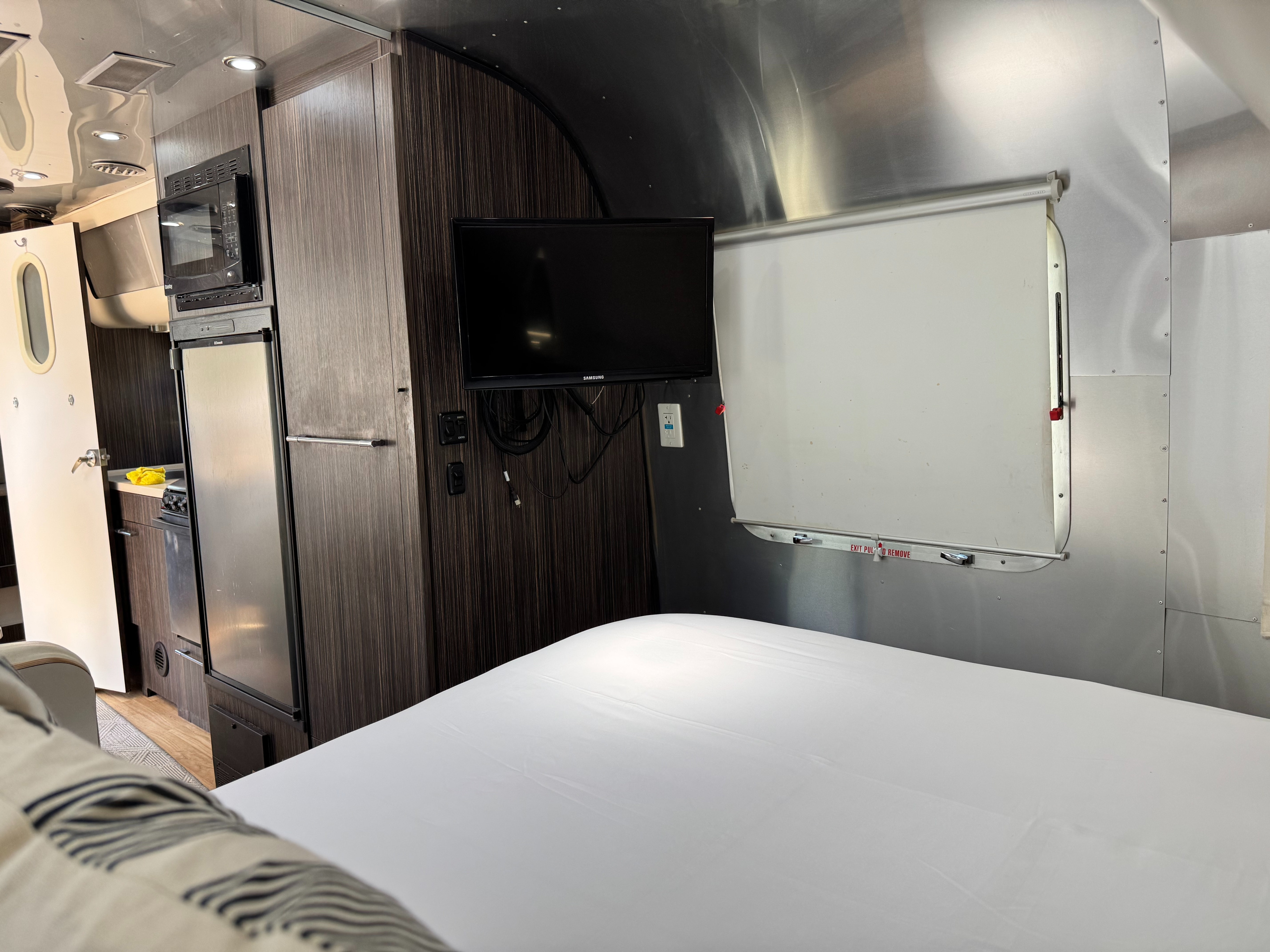 Inside a sleek rv rental: bedroom with white sheets, compact kitchen, and TV. Ideal for road trips!. Airstream International 2017