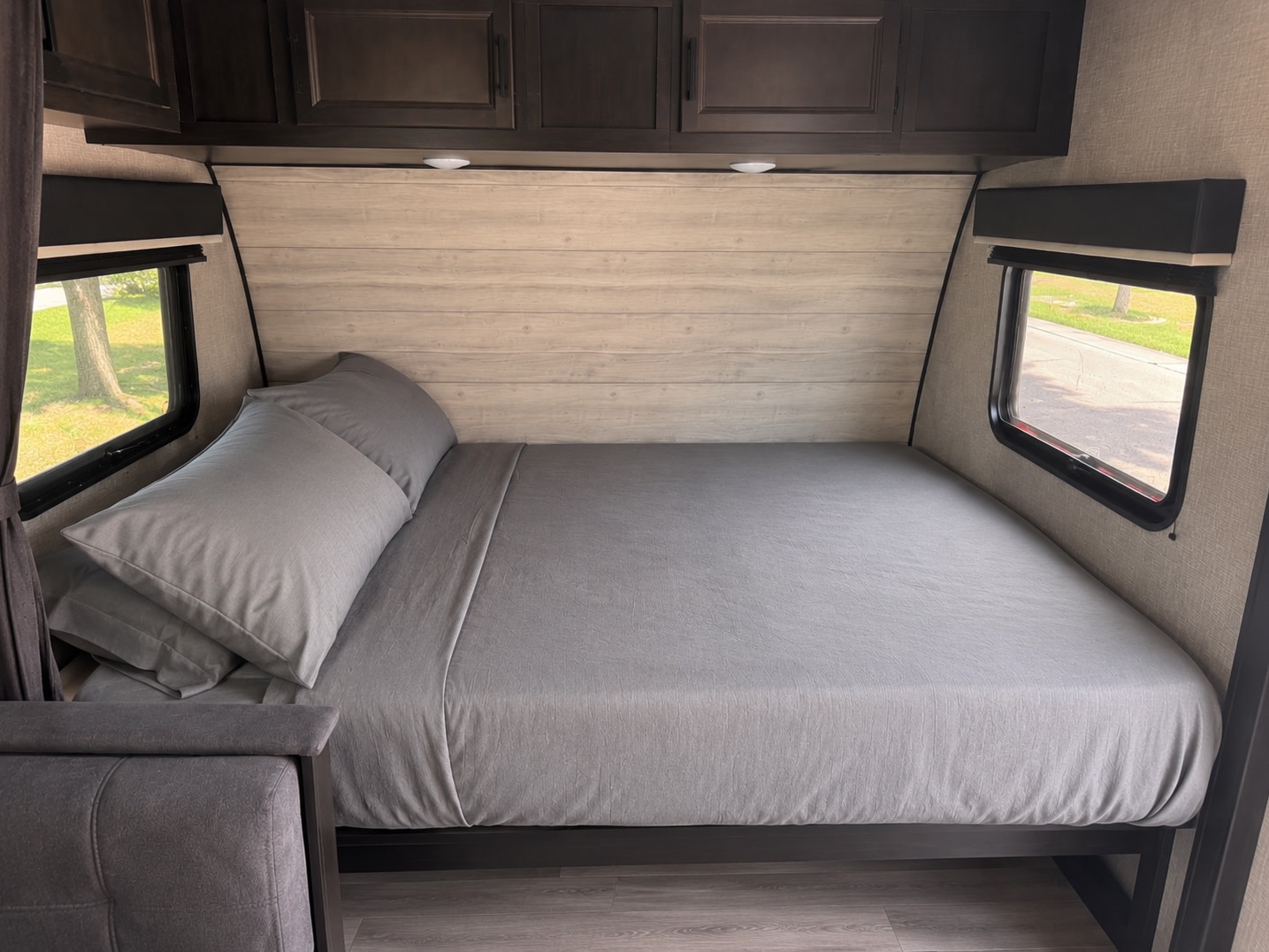 This inviting RV rental bedroom features a comfortable bed with crisp gray sheets, dark wood cabinets, and bright windows.. Jayco Jay Flight SLX Baja Edition 2023