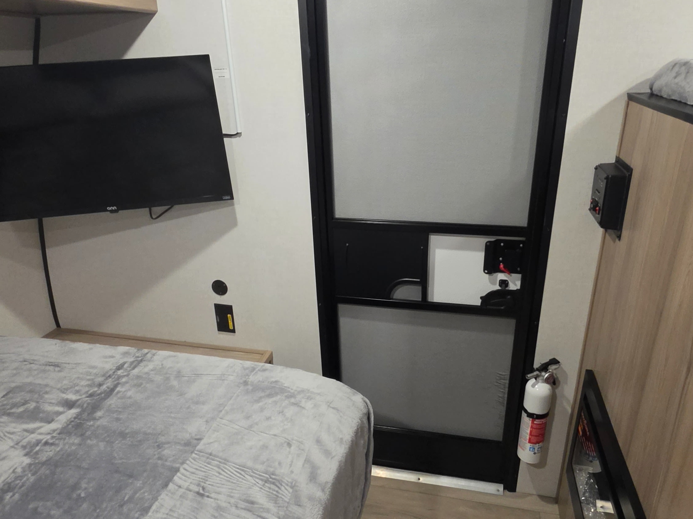 RV rental bedroom with a wall-mounted TV, cozy bed, and an entry door with a fire extinguisher for safety.. Keystone RV Coleman 2026