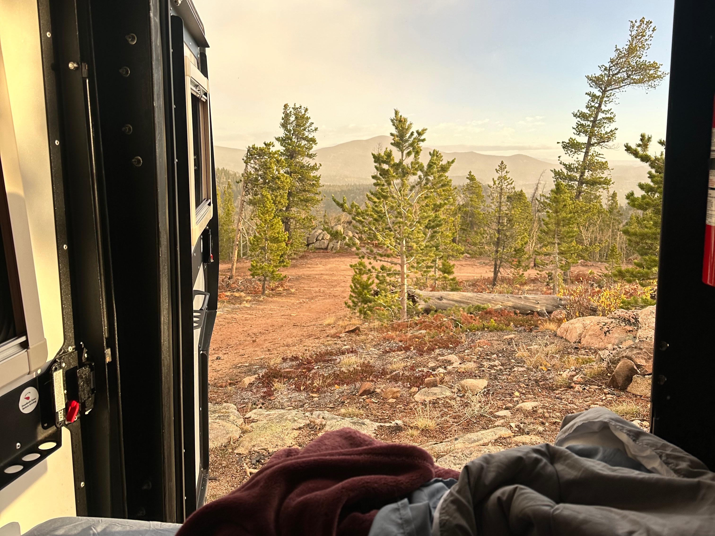 Cozy rv rental view from bed: tranquil mountains, pine trees, and a clear sky for your outdoor adventure.. TAXA Tiger Moth 2021