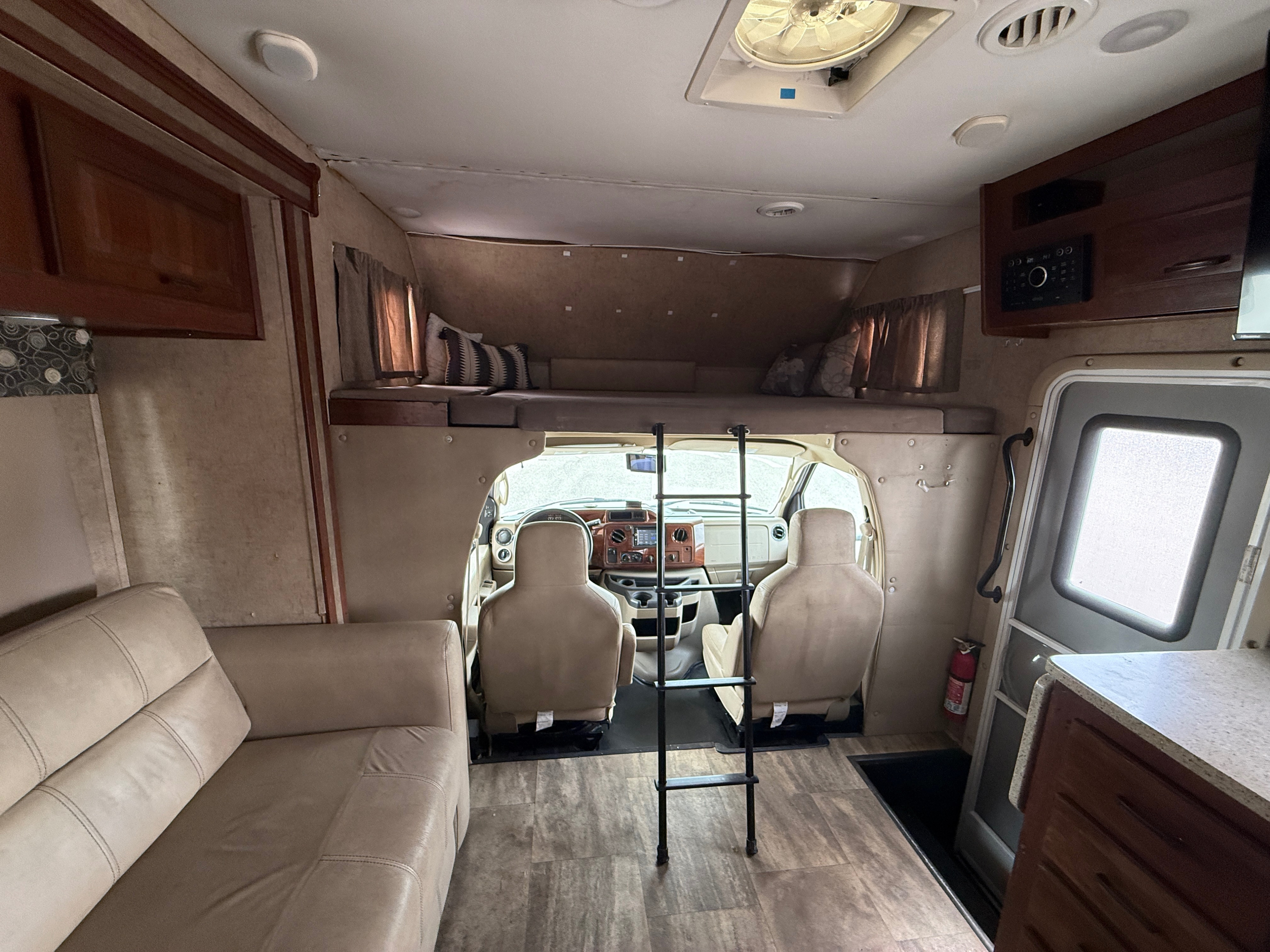 Interior of an RV rental showing the living space, front cockpit, sofa, and overhead bunk with ladder for sleeping.. Forester Forester Motorhome 2016